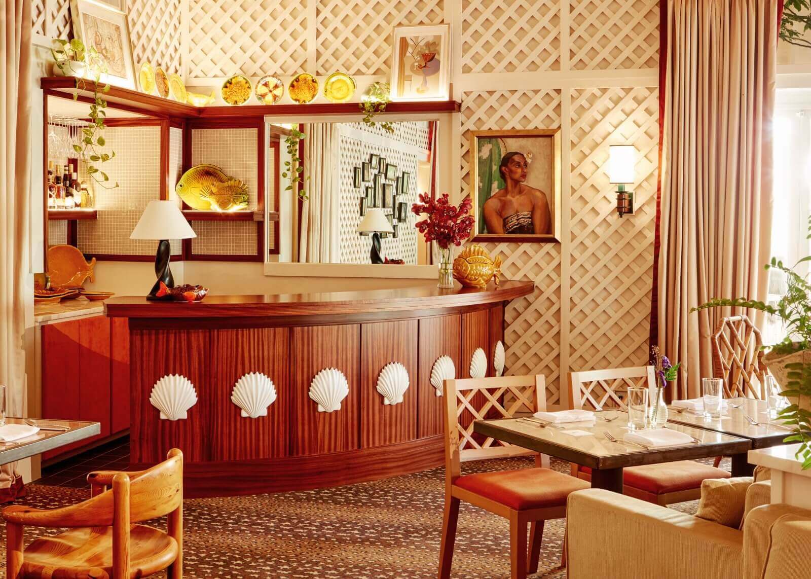 Tillies, North America — Art Deco cocktail bar with burgundy lacquered reception desk, shell motifs, brass accents, geometric wall paneling, and warm amber lighting.