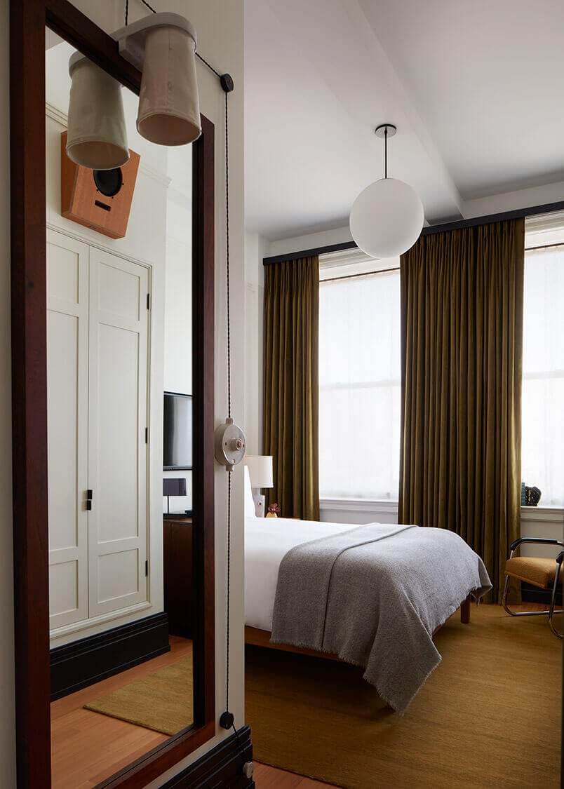 Nine Orchard, North America — Modern hotel bedroom with olive curtains, pendant lighting, wooden flooring, and mirrored entryway.