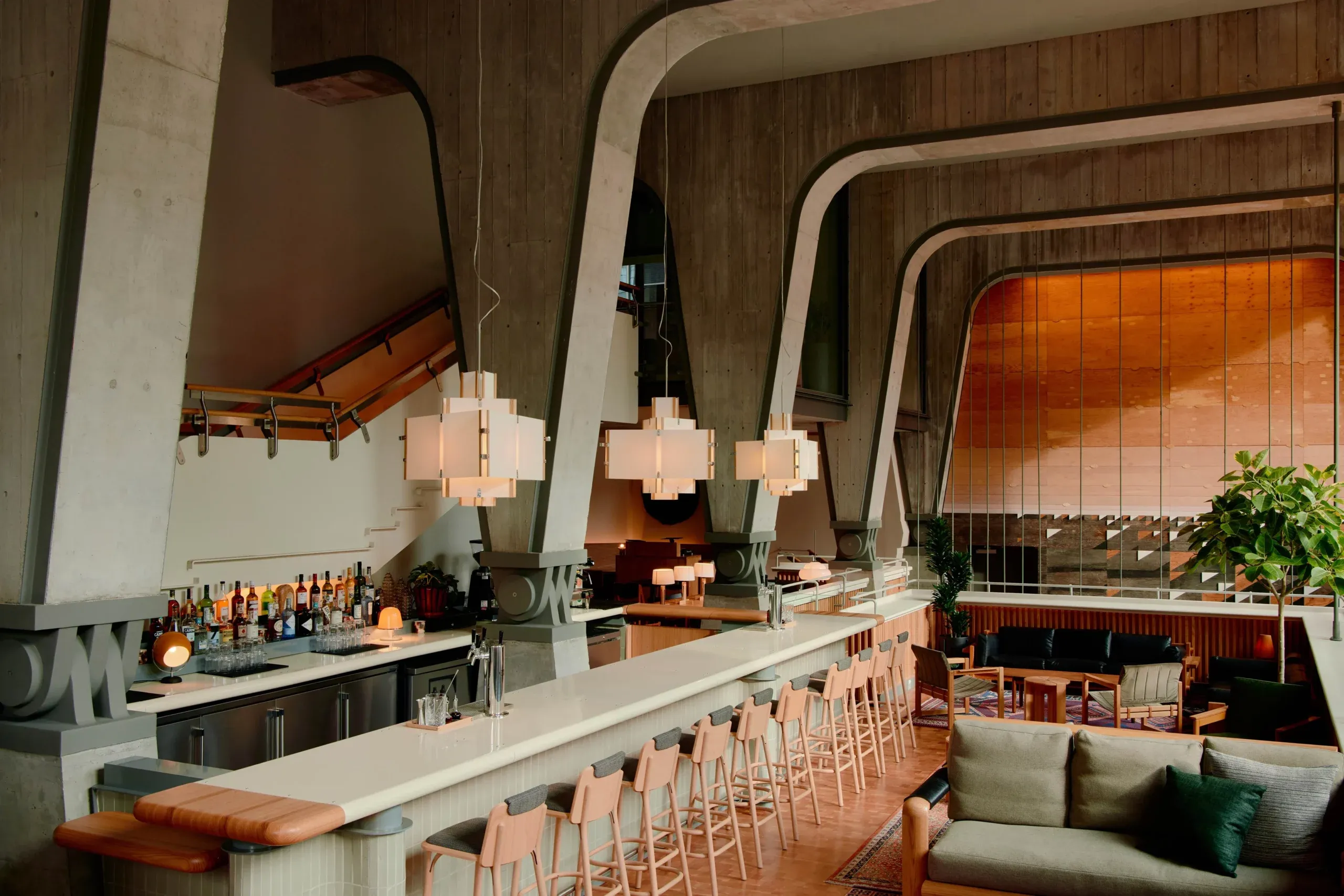 Ace Hotel Toronto, Canada — Brutalist concrete bar with curved soffits, terrazzo countertop, coral leather seating, and floor-to-ceiling amber glass overlooking dining room.