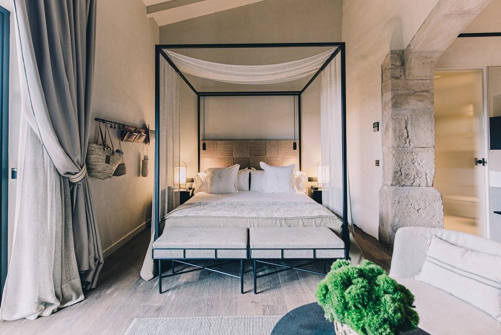 Can Ferrereta, Balearic Islands — Canopy bed with black metal frame, linen drapes, stone walls, and neutral palette in luxury bedroom suite.