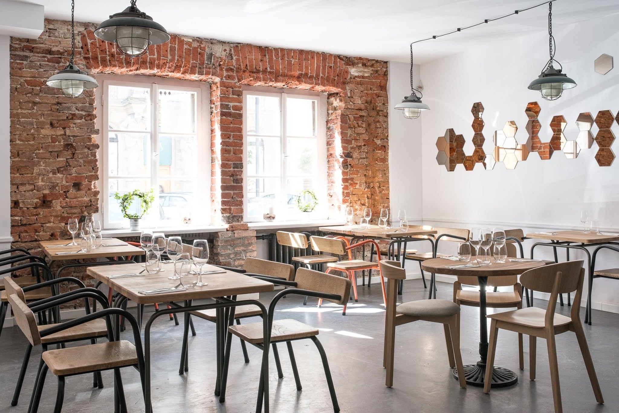 Alewino, Europe — Industrial brick dining room with wooden tables, pendant lights, and hexagonal wall art installation overlooking street windows.