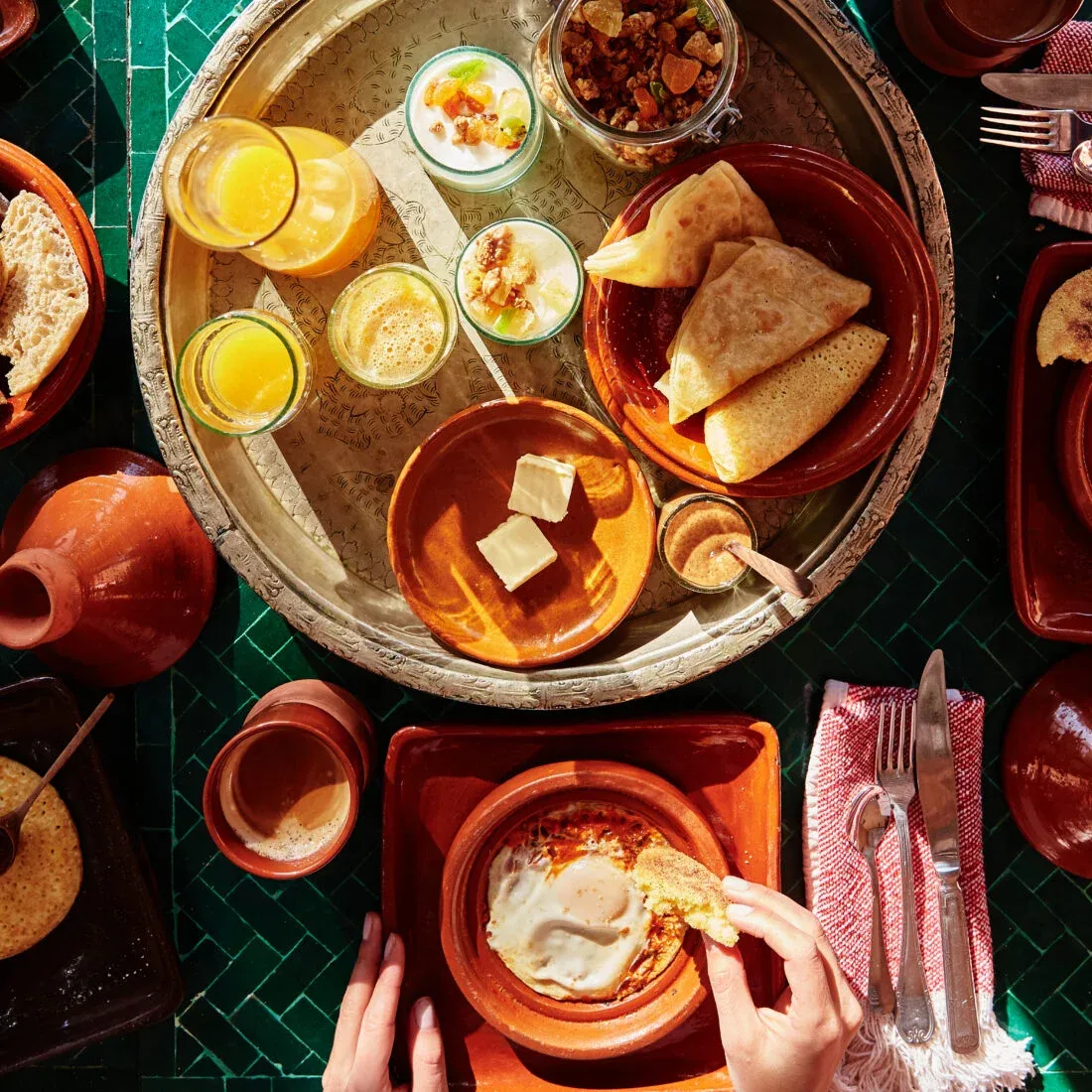 El Fenn, Africa — Overhead breakfast spread with terracotta ceramics, fresh crepes, orange juice, and traditional Moroccan dishes on green tile.