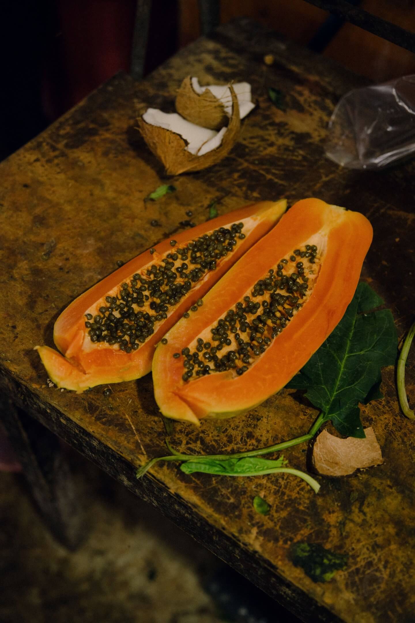 Tulum Treehouse, Mexico — Halved papaya with black seeds and tropical foliage on weathered wooden surface, natural light.