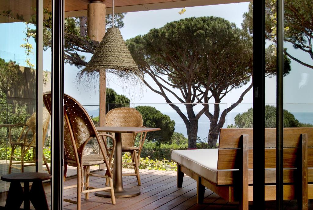 Lily of the Valley, Europe — Coastal terrace with woven chair, wooden bench, straw hat, and Italian stone pine trees framing Mediterranean sea view.