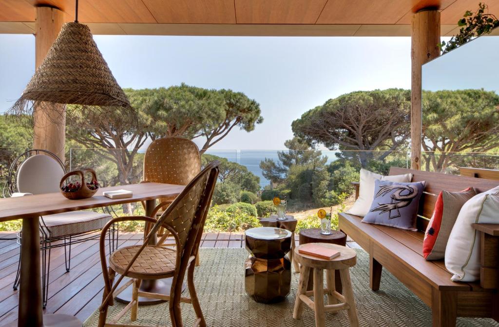 Lily of the Valley, Europe — Mediterranean terrace with woven pendant light, wooden furniture, sea views through pine trees, natural materials and coastal modernism.