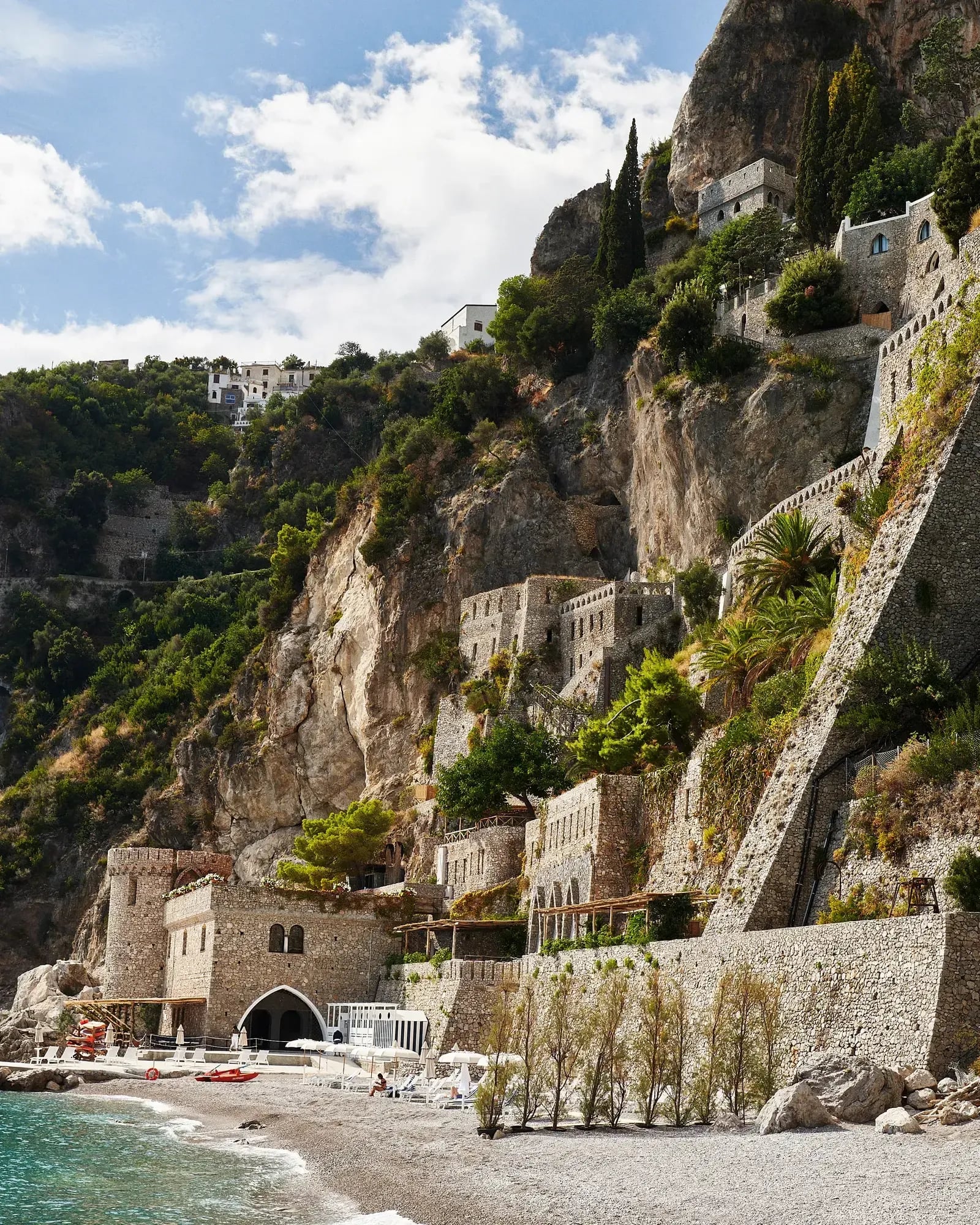 Borgo Santandrea, Italy — Clifftop stone fortress with terraced architecture, carved into dramatic limestone, overlooking turquoise Mediterranean waters and pebble beach.