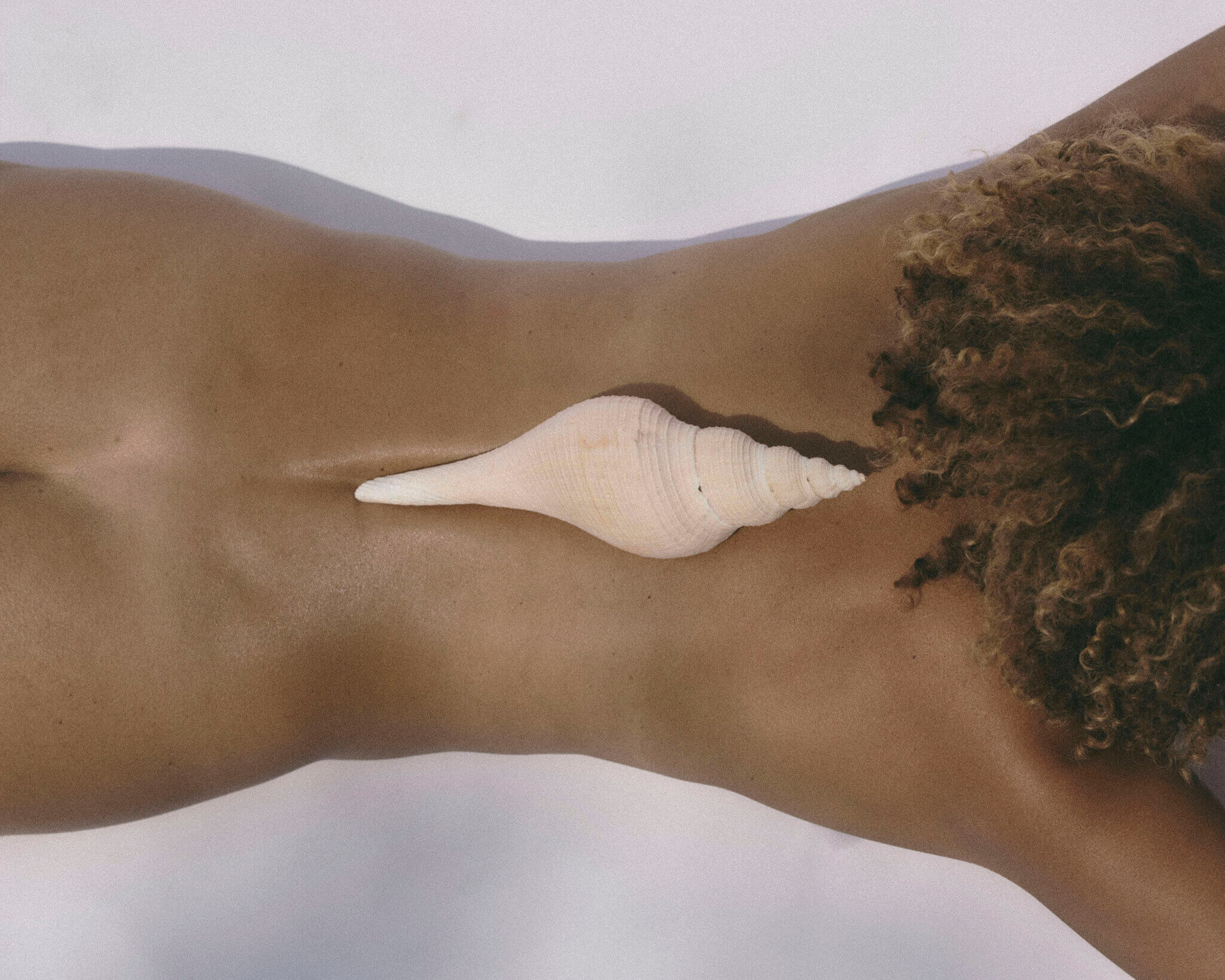 Retreats — Minimalist desert landscape with cream-colored seashell on sand, sculptural rock formation, muted earth tones, serene luxury aesthetic.