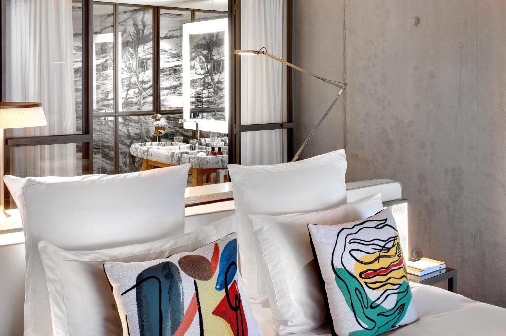 Lily of the Valley, Europe — Minimalist bedroom with artisan pillows, floor-to-ceiling windows overlooking snowy landscape, concrete walls, brass reading lamp, contemporary luxury design.