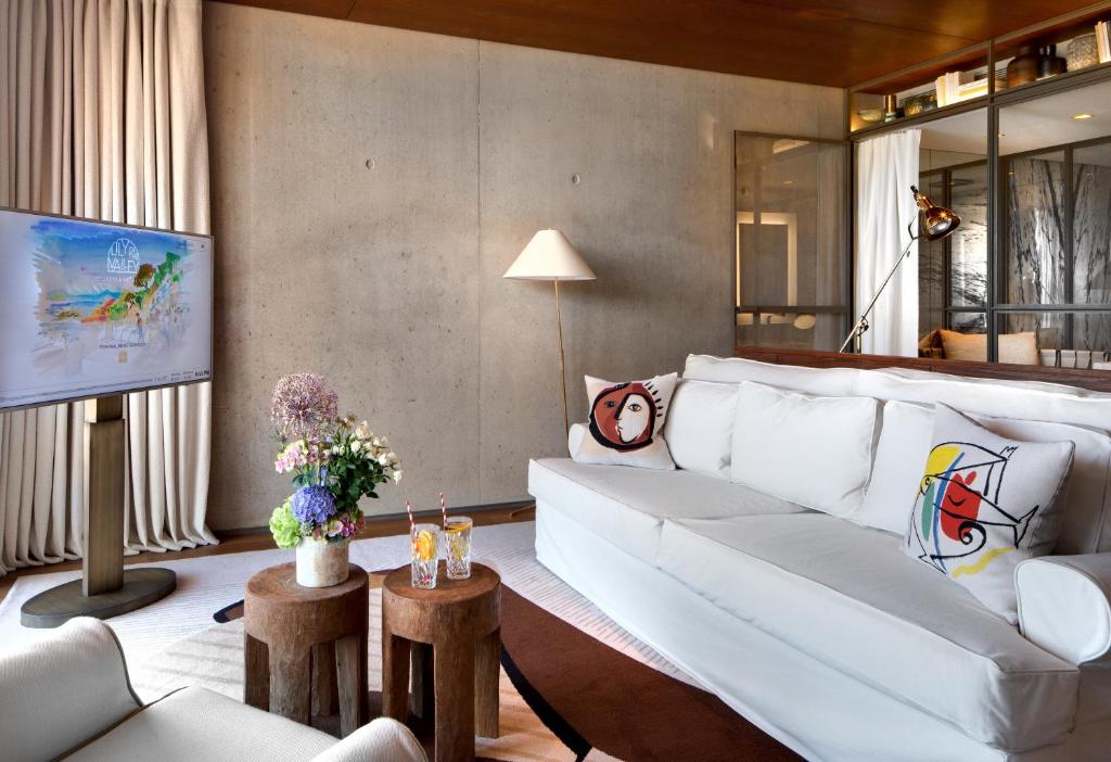 Lily of the Valley, Europe — Concrete bedroom with white upholstered bed, wooden side tables, pendant lighting, and floor-to-ceiling windows overlooking landscape.
