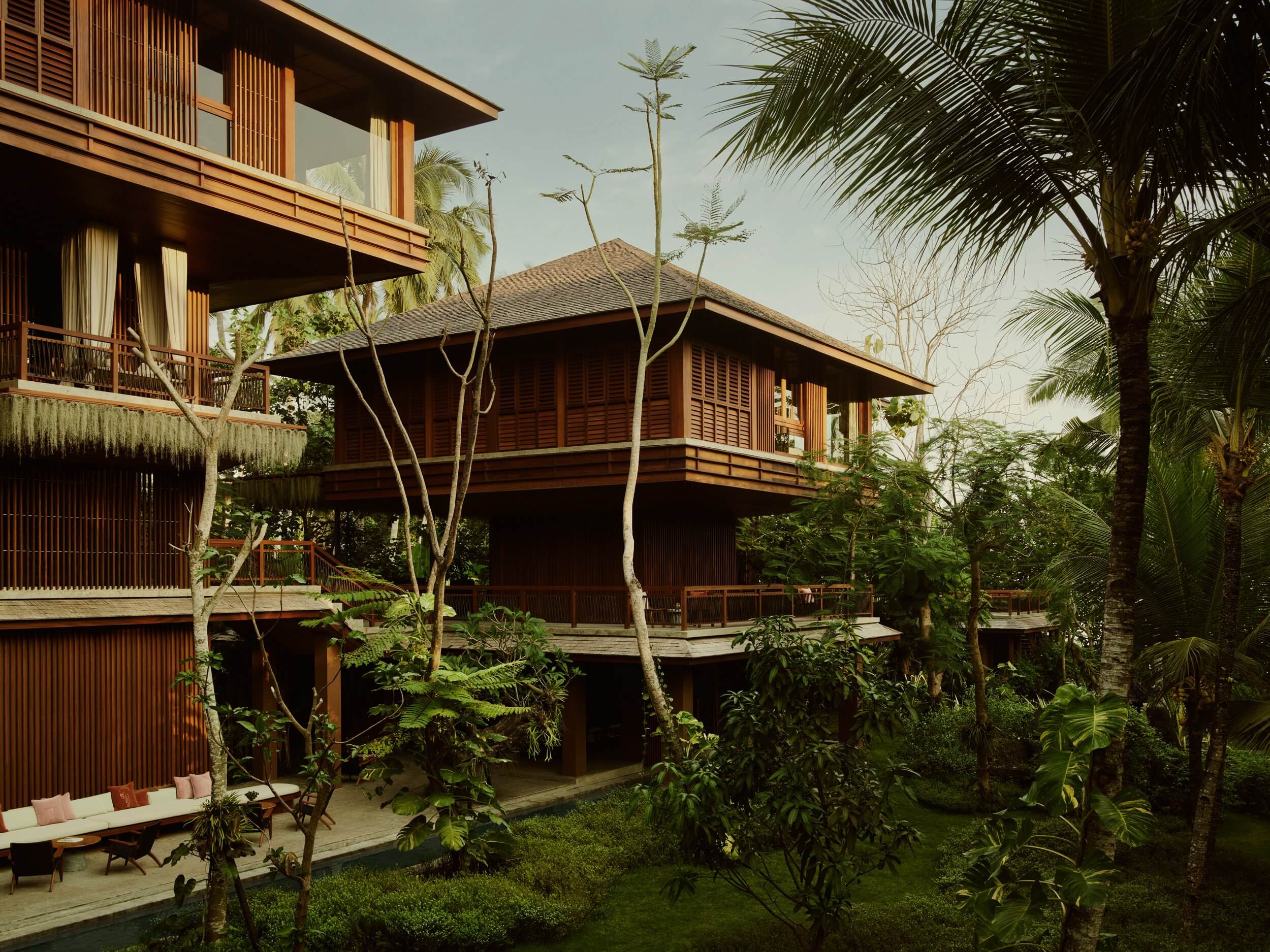Lost Lindenberg, Asia — Timber-clad tropical villa with expansive covered pavilions, lush palm garden, and layered wooden louvers catching golden afternoon light.