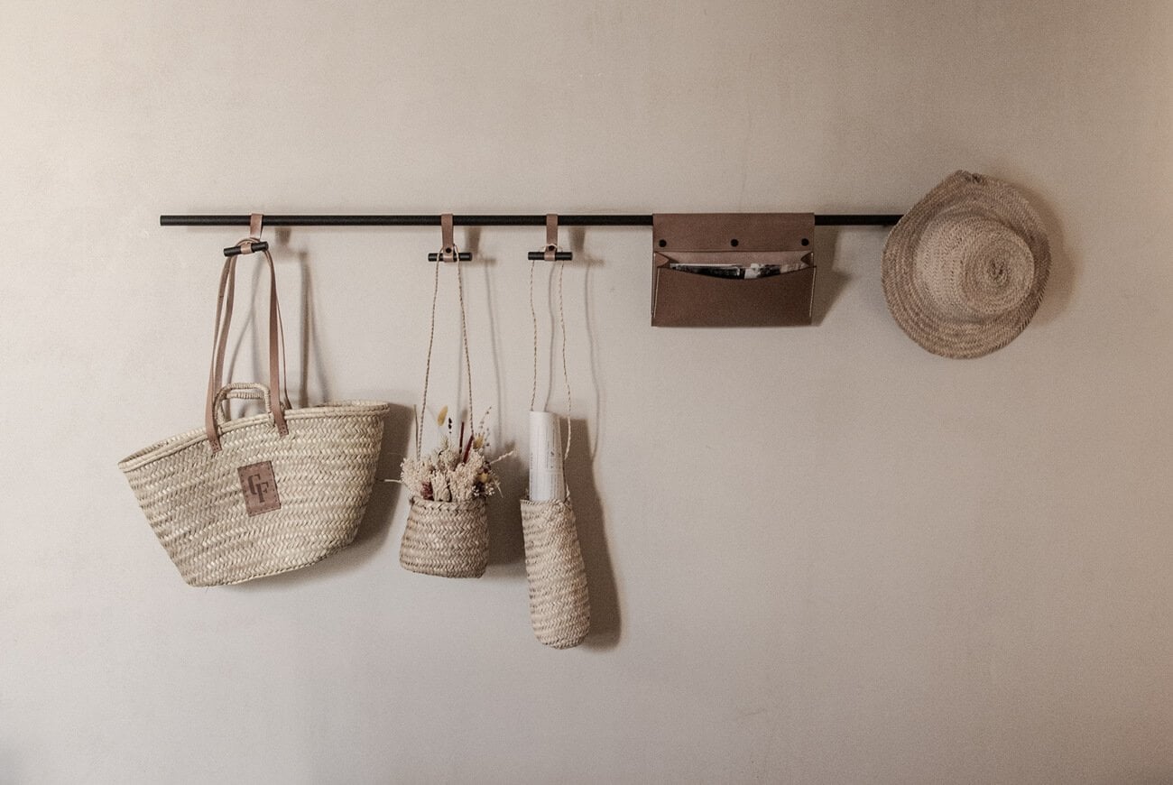 Can Ferrereta, Balearic Islands — Woven baskets and dried florals hung on black rod against cream wall, natural fiber storage organization.