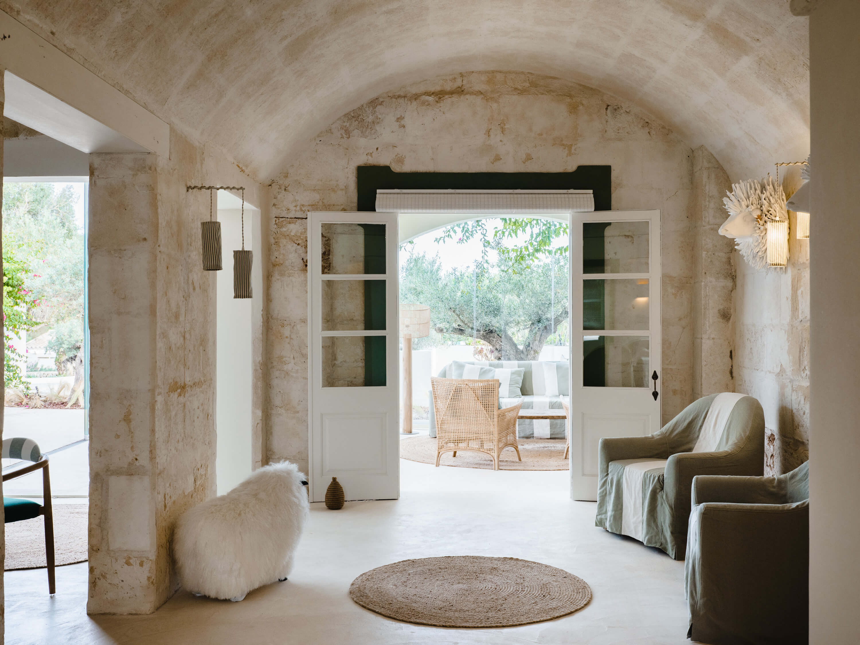 Morvedra Nou, Balearic Islands, Spain — Barrel-vaulted stone room with white French doors opening to terrace, natural light, linen furnishings, minimalist Mediterranean design.