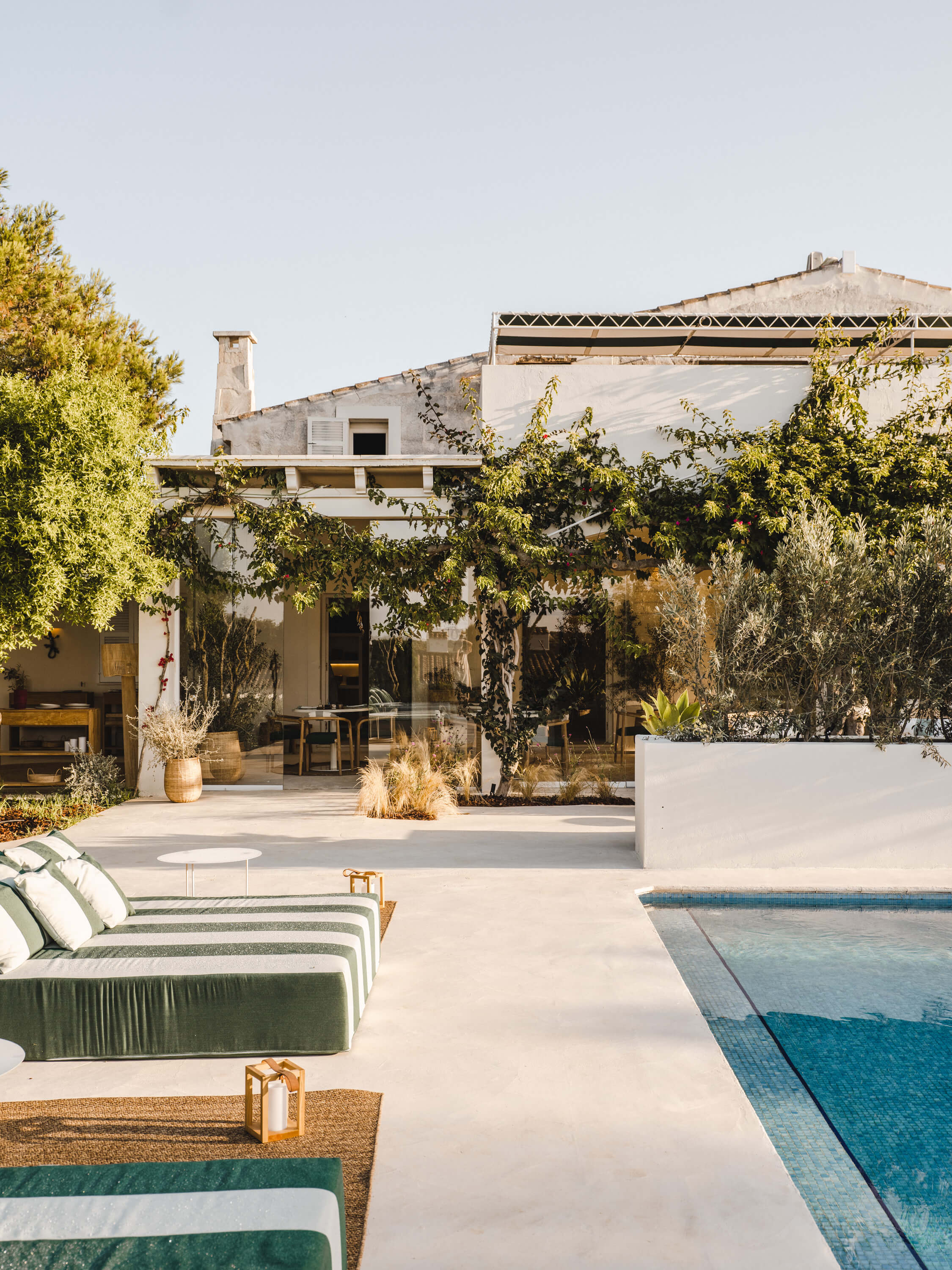 Morvedra Nou, Balearic Islands — Mediterranean courtyard with limestone terrace, striped loungers, turquoise pool, and whitewashed architecture framed by drought-resistant greenery.
