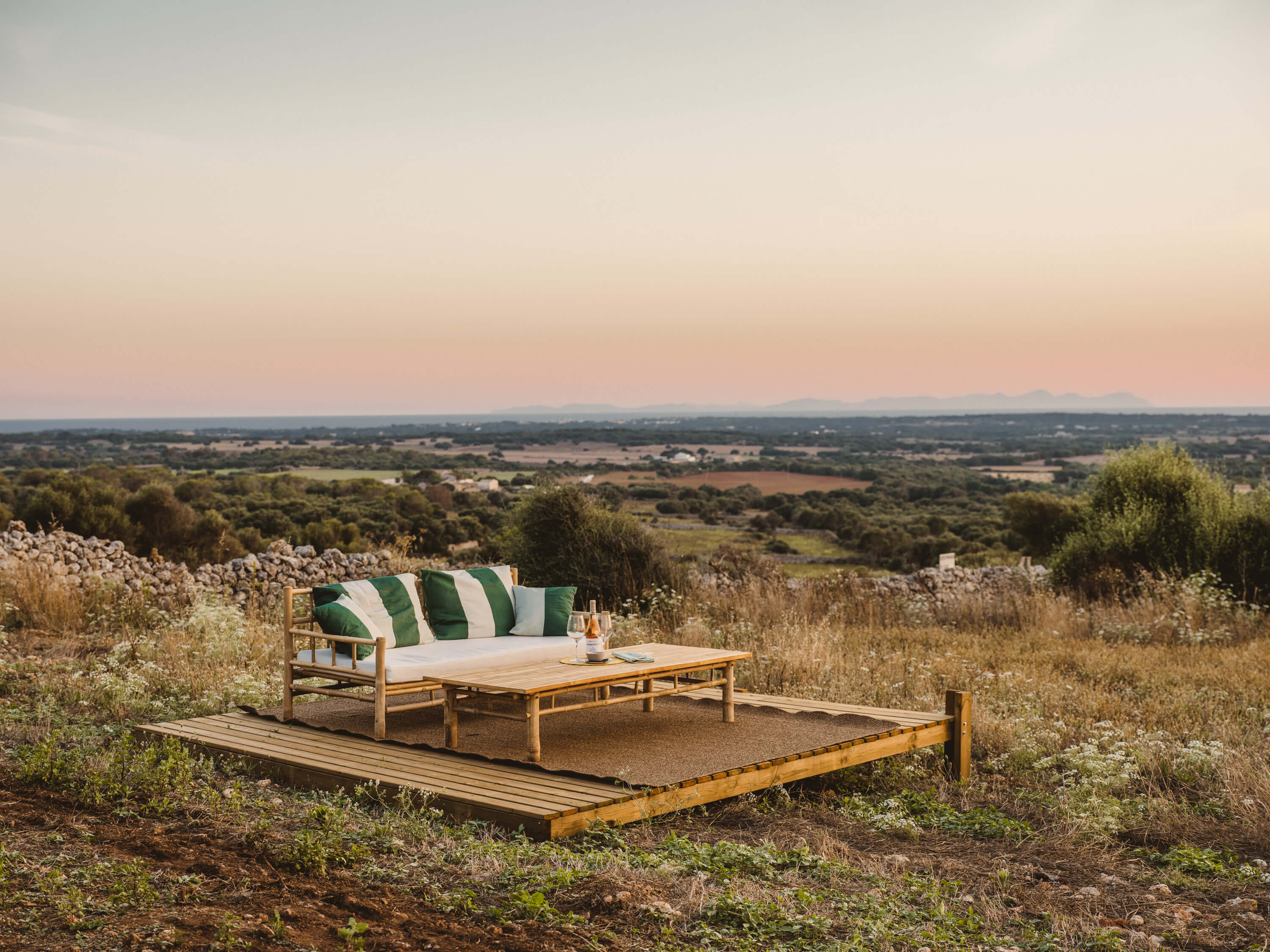 Morvedra Nou, Balearic Islands — Wooden daybed with striped green cushions on terrace overlooking rolling countryside at sunset.