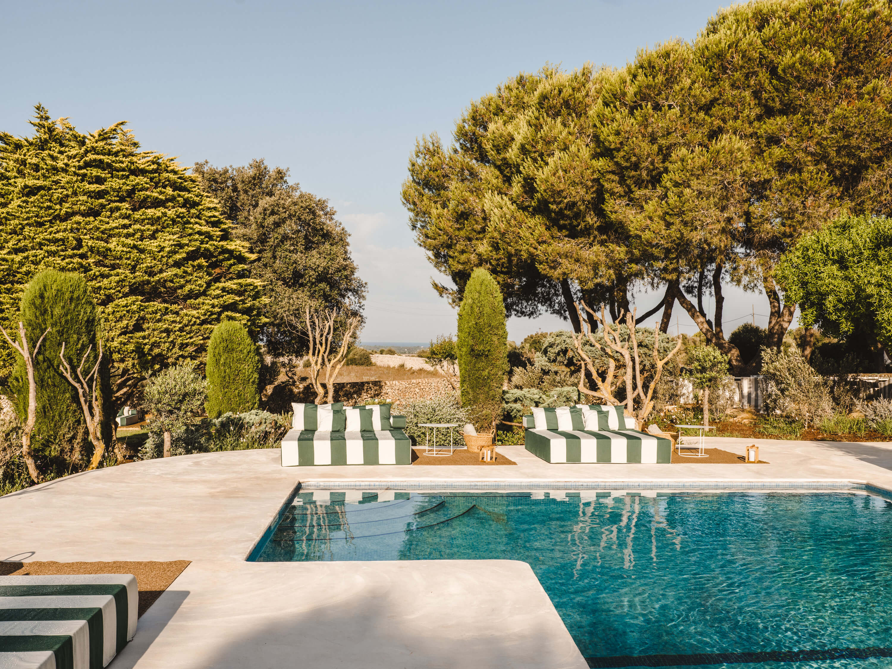 Morvedra Nou, Balearic Islands, Spain — striped sun loungers by turquoise pool overlooking Mediterranean landscape, cypress and pine trees, limestone terrace.