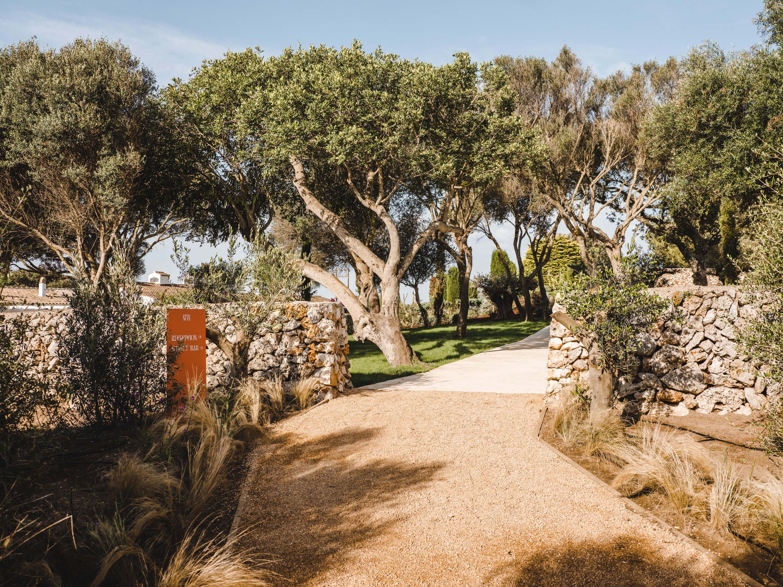 Morvedra Nou, Balearic Islands, Spain — Tree-lined gravel driveway with stone walls and Mediterranean landscaping leading to luxury property entrance.