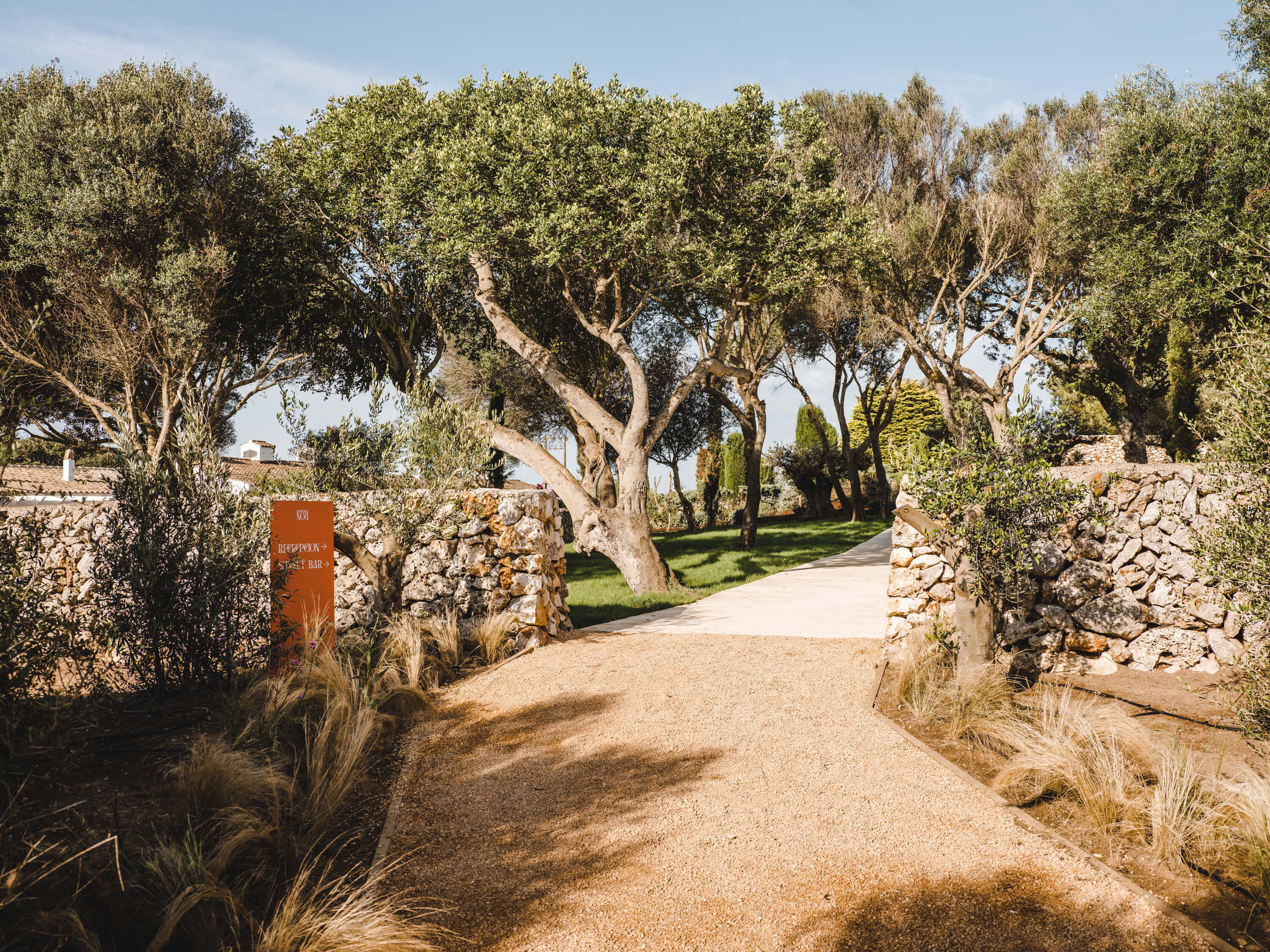 Morvedra Nou, Balearic Islands, Spain — Tree-lined gravel driveway with stone walls and Mediterranean landscaping leading to luxury property entrance.