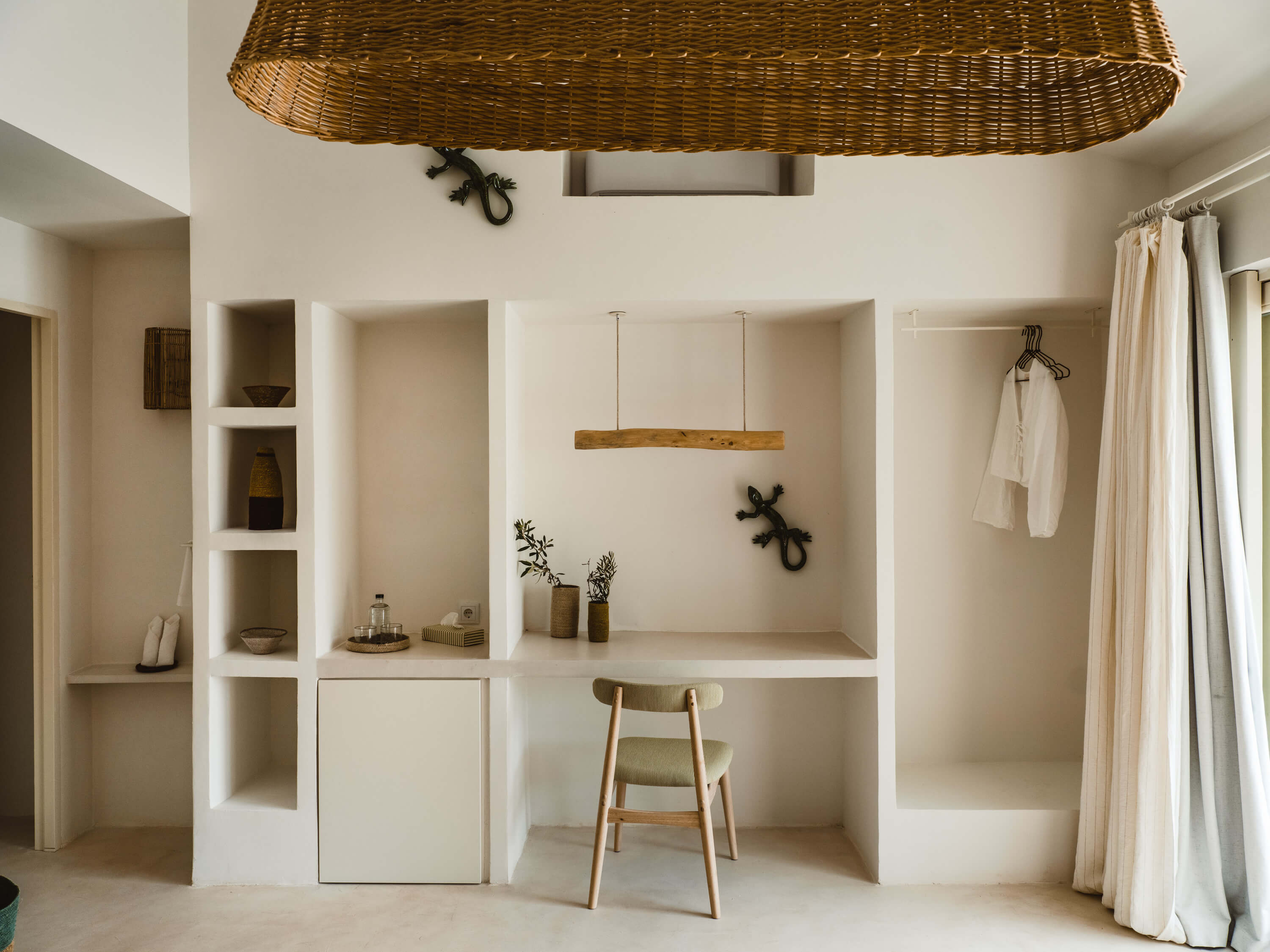 Morvedra Nou, Balearic Islands — Minimalist white built-in shelving with natural wood accents, woven pendant light, and linen curtains creating serene Mediterranean workspace.