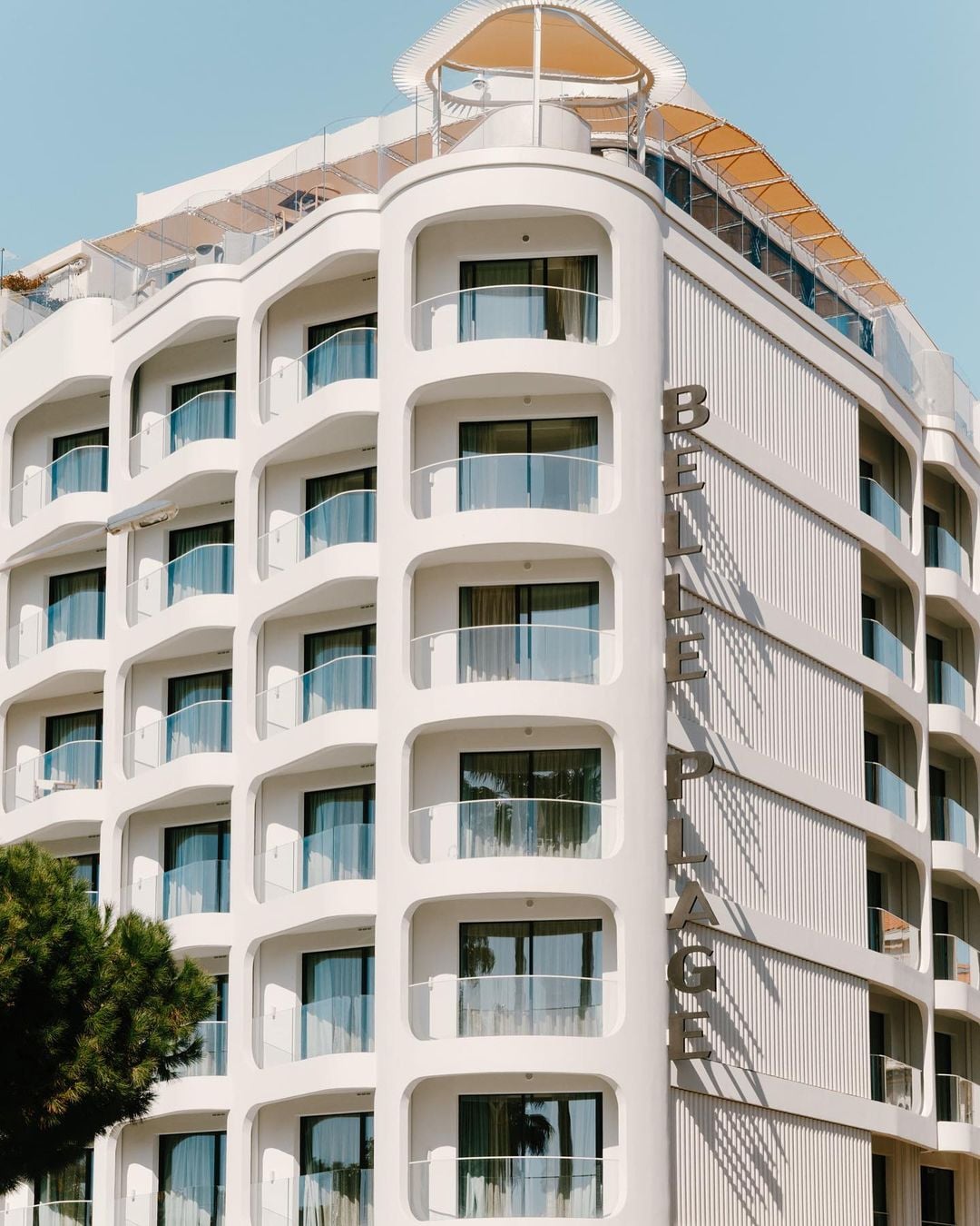Belle Plage, Europe — White modernist hotel facade with curved balconies, floor-to-ceiling windows, and geometric metal railings under clear sky.