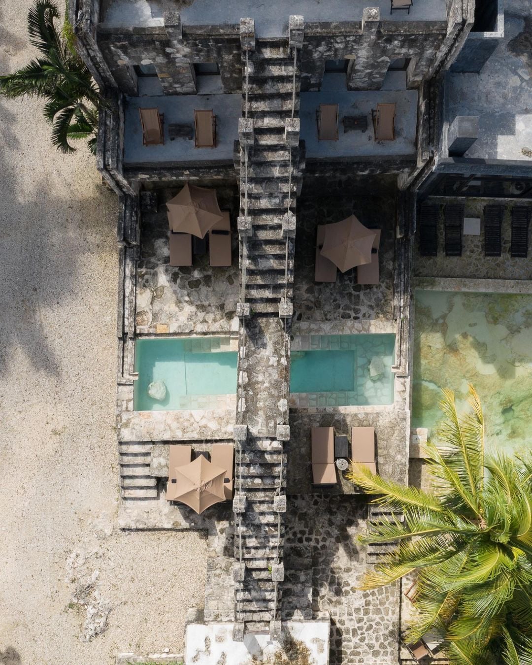 Coqui Coqui Papholchac, Mexico — Aerial view of stone courtyard with turquoise pools, tan loungers, and palapa umbrellas nestled between colonial architecture.