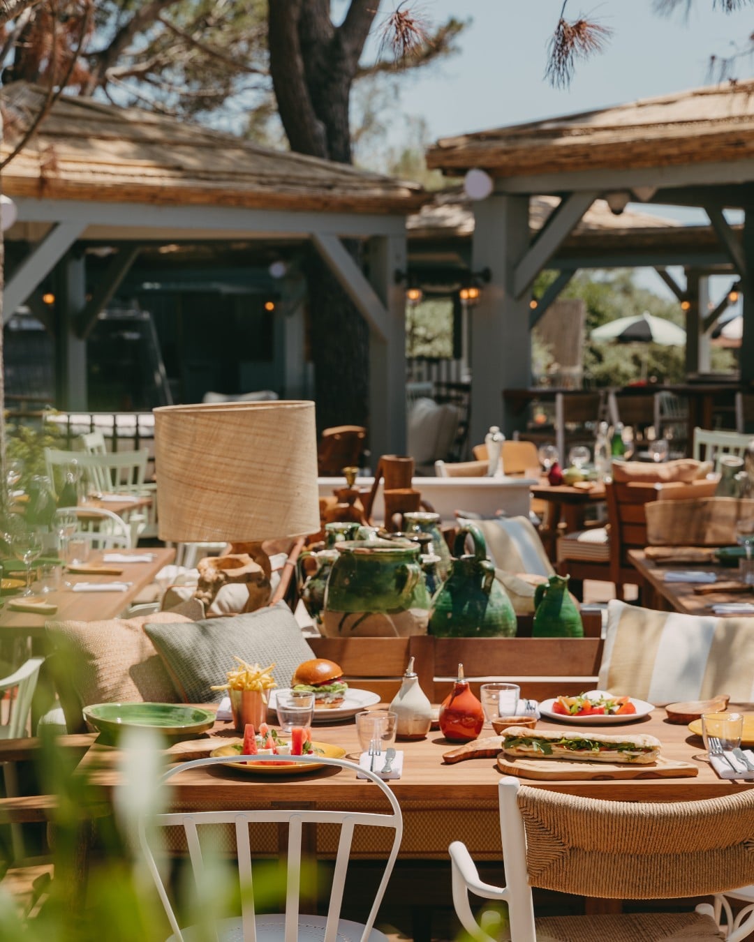 Lily of the Valley, Europe — Outdoor dining terrace with wooden pergola, linen-upholstered chairs, potted plants, and natural light filtering through timber beams.