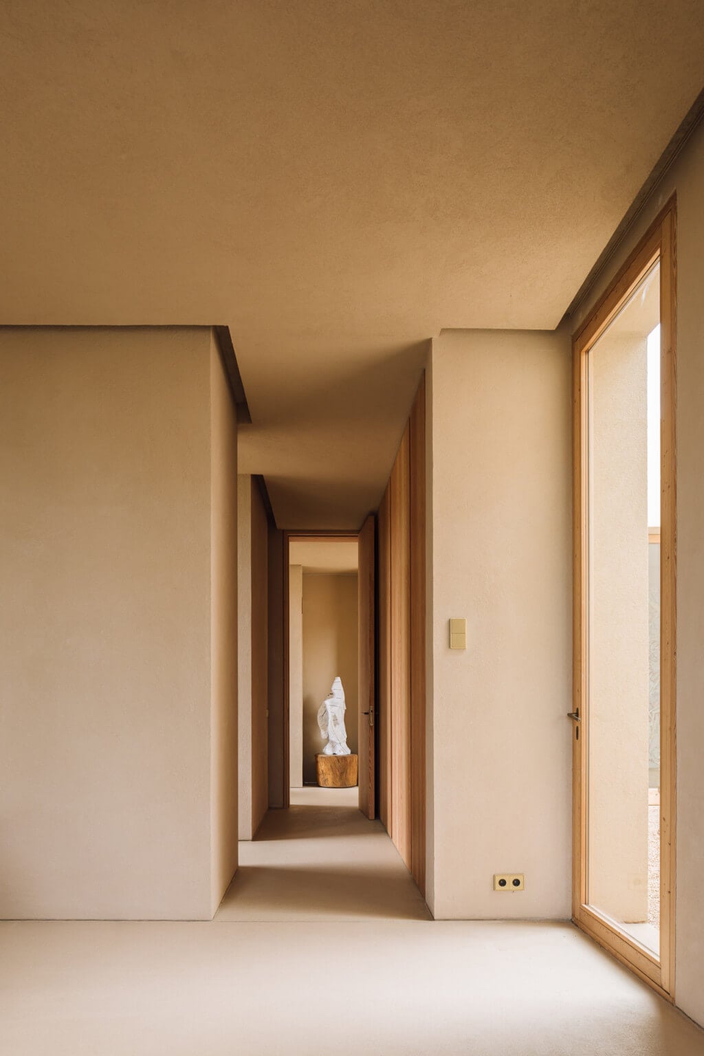 Melides Art, Portugal — Minimalist hallway with natural light, wooden frames, cream walls, sculptural figure in niche, gallery aesthetic.