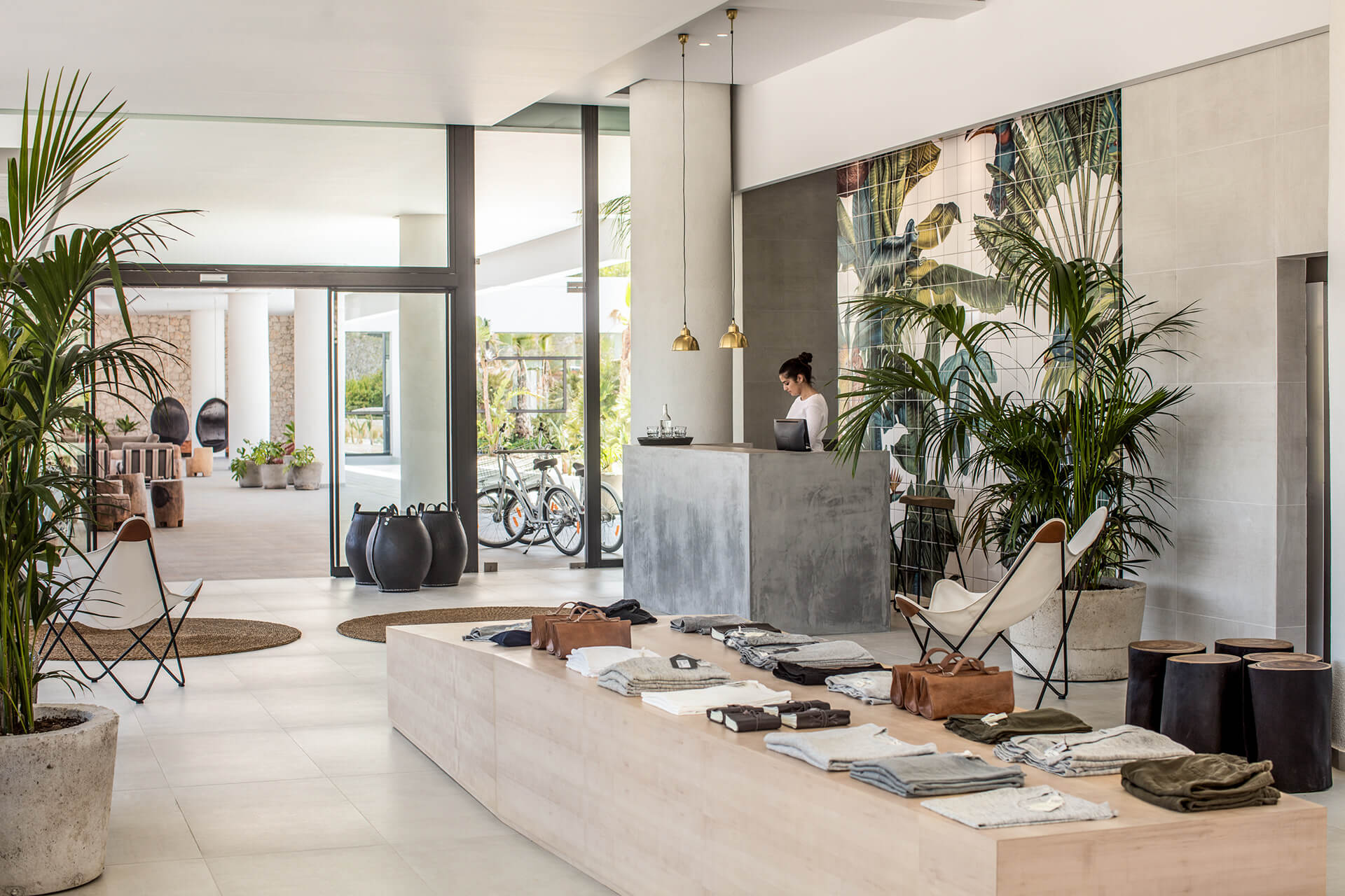 Casa Cook Rhodes, Greece — Modern hotel lobby with concrete reception desk, potted palms, natural light, minimalist furnishings, and curated retail display.