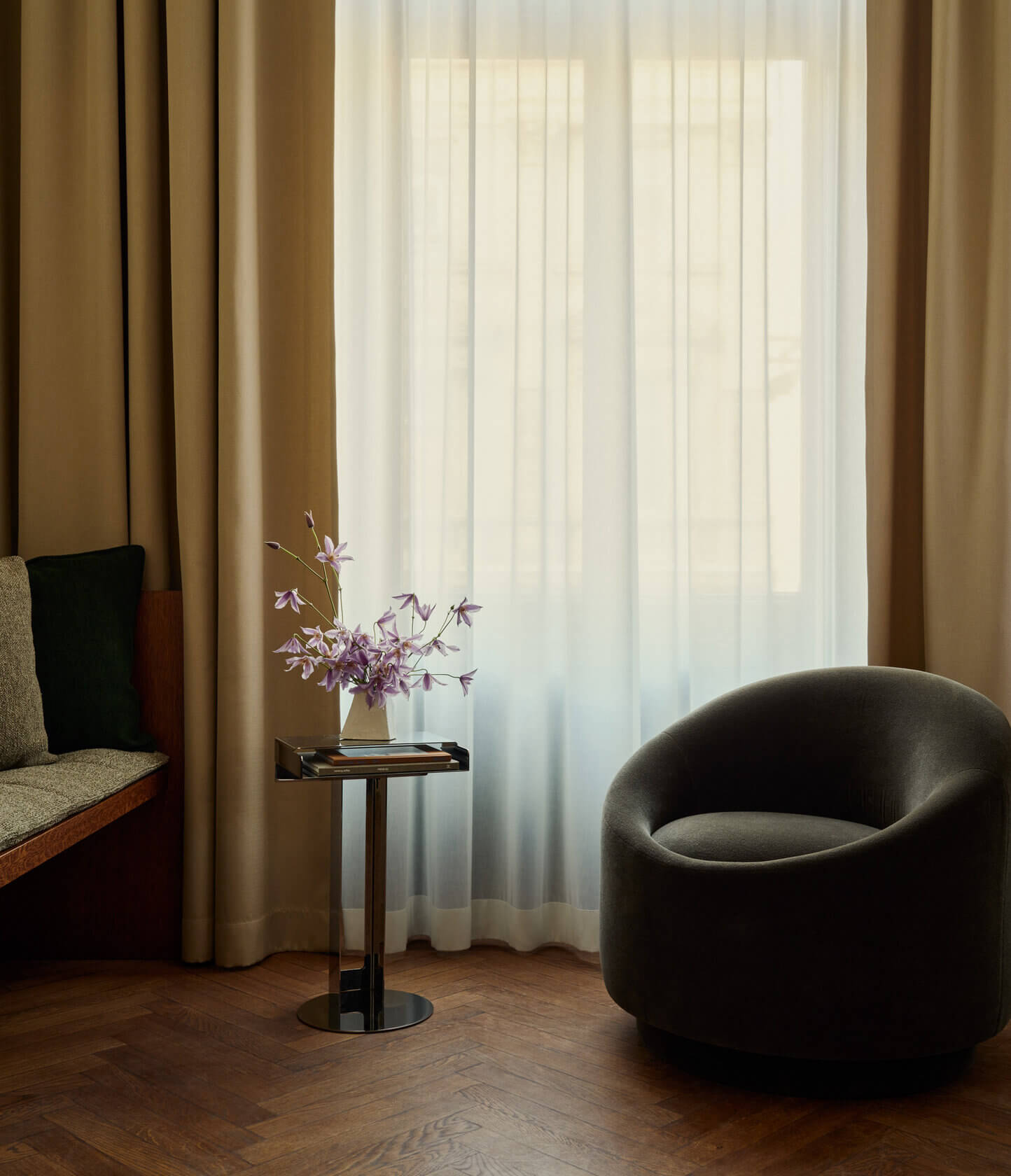 Château Royal, Europe — Modern lounge with curved charcoal armchair, side table with purple flowers, warm curtains, parquet flooring, and soft natural light.