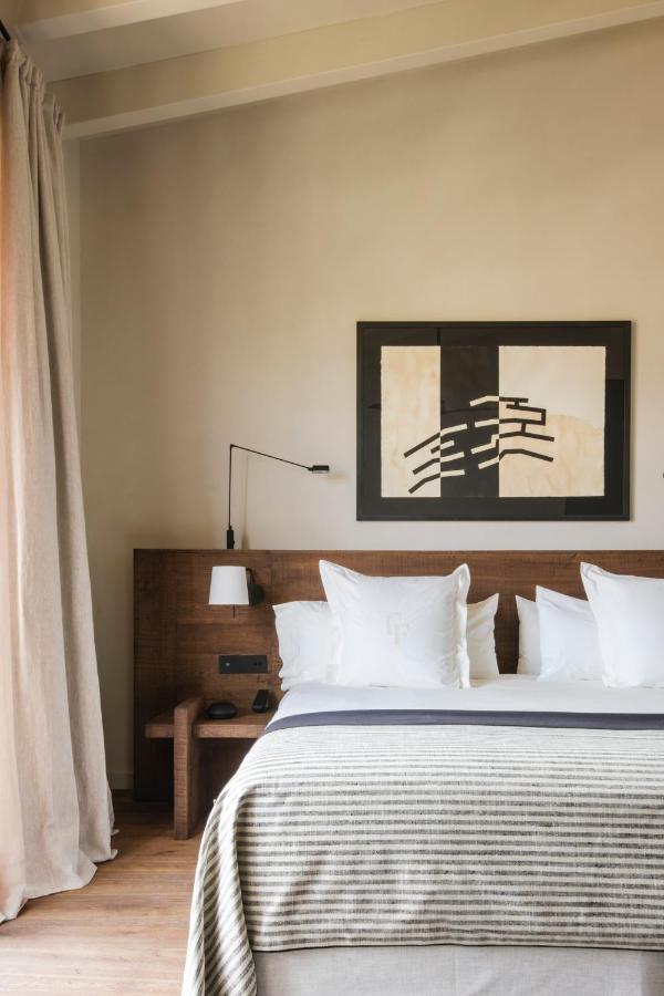 Can Ferrereta, Balearic Islands — Minimalist bedroom with walnut headboard, white linens, striped throw, modernist black wall art, warm natural light, wooden floors.