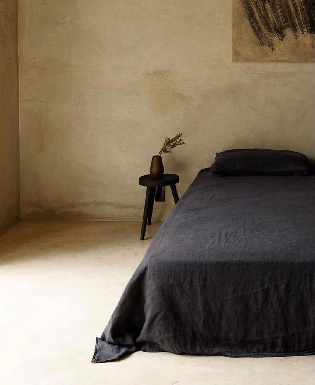 Villa ITO, Mexico — Minimalist bedroom with charcoal linen bed, dark wooden nightstand, dried botanicals, concrete walls, and soft natural light.