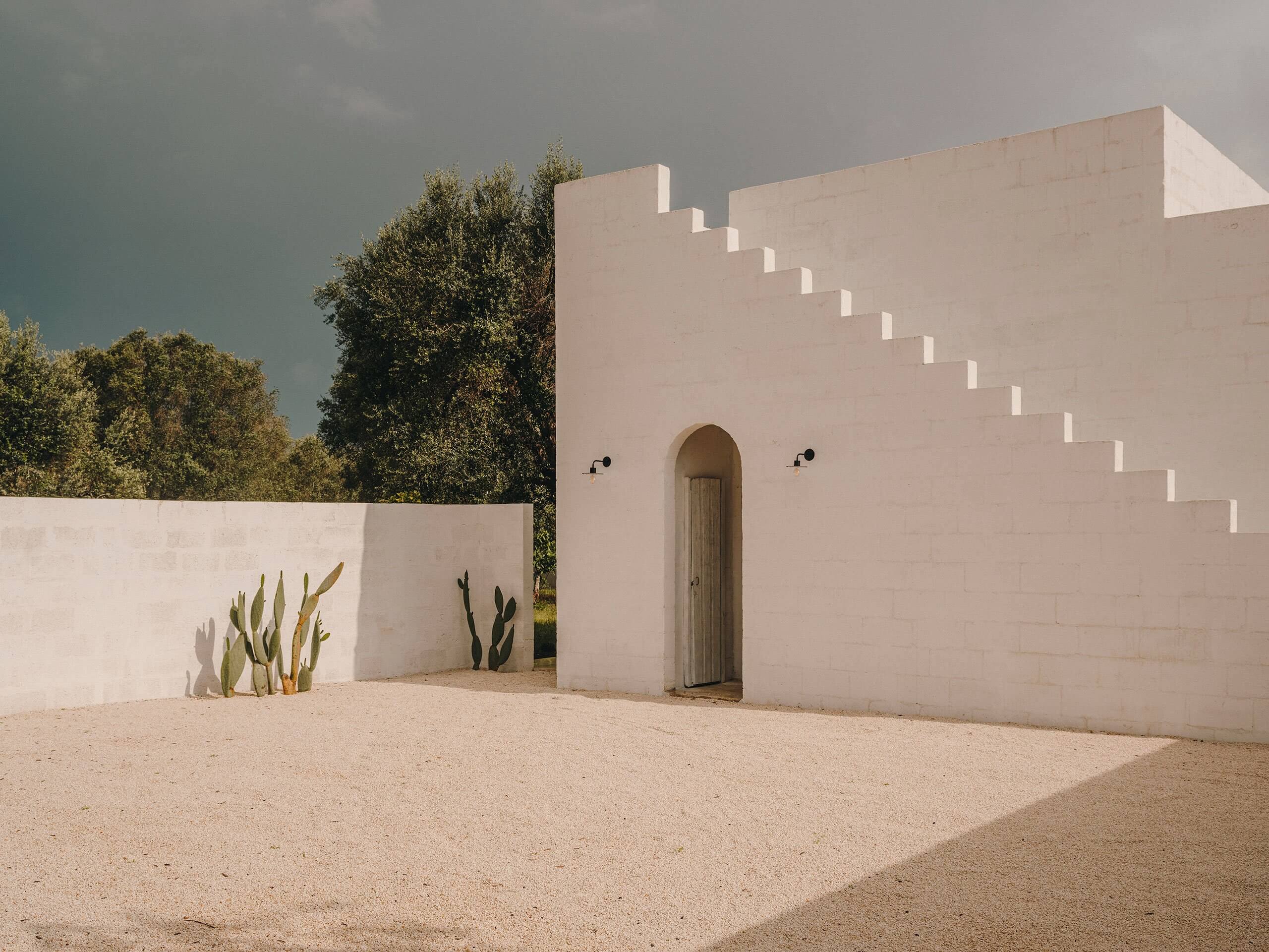 Borgo Gallana, Europe — Minimalist whitewashed villa with arched doorway, stepped roofline, and desert landscaping against clear sky.