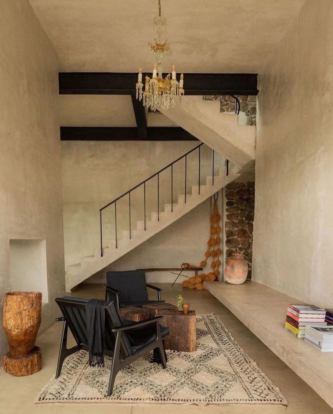 Villa ITO, Mexico — Minimalist staircase with concrete walls, black steel railing, crystal chandelier, and curated furnishings beneath floating beam detail.