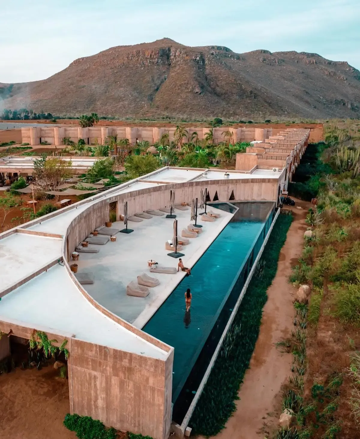 Paradero Todos Santos, Mexico — Terracotta resort with curved pool, loungers, and mountain backdrop in desert landscape.