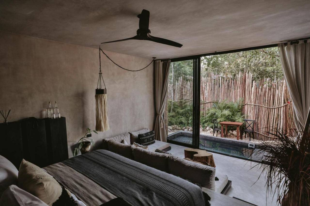 Bardo, Mexico — Modern bedroom with black ceiling fan, concrete walls, charcoal bedding, and floor-to-ceiling glass doors opening to forest pool terrace.