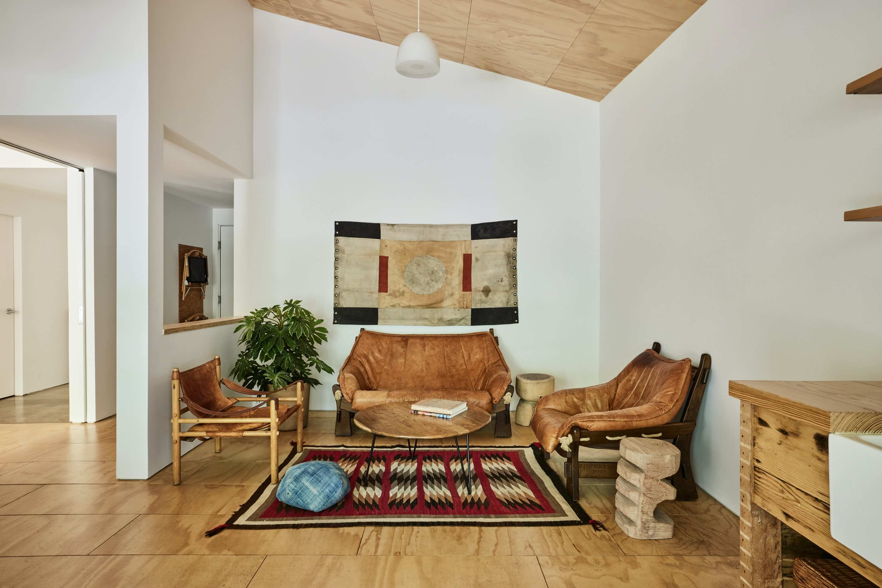 Tourists, North America — Mid-century modern living room with cognac leather slingback chairs, geometric textile art, wooden ceiling, and Southwestern rug on blonde wood flooring.