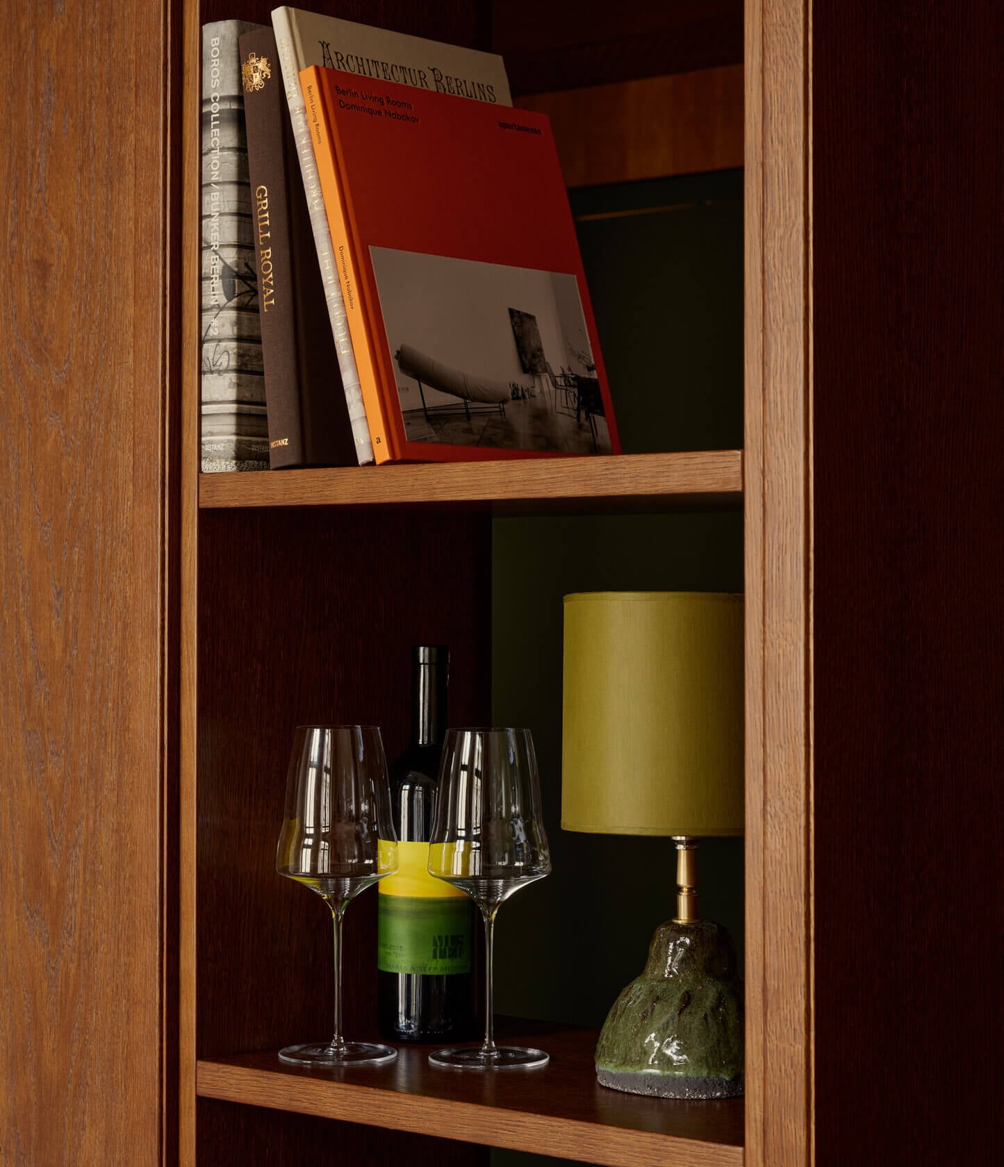 Château Royal, Europe — Wooden shelving with architecture books, wine bottle, glasses, and sculptural decor against deep burgundy interior.