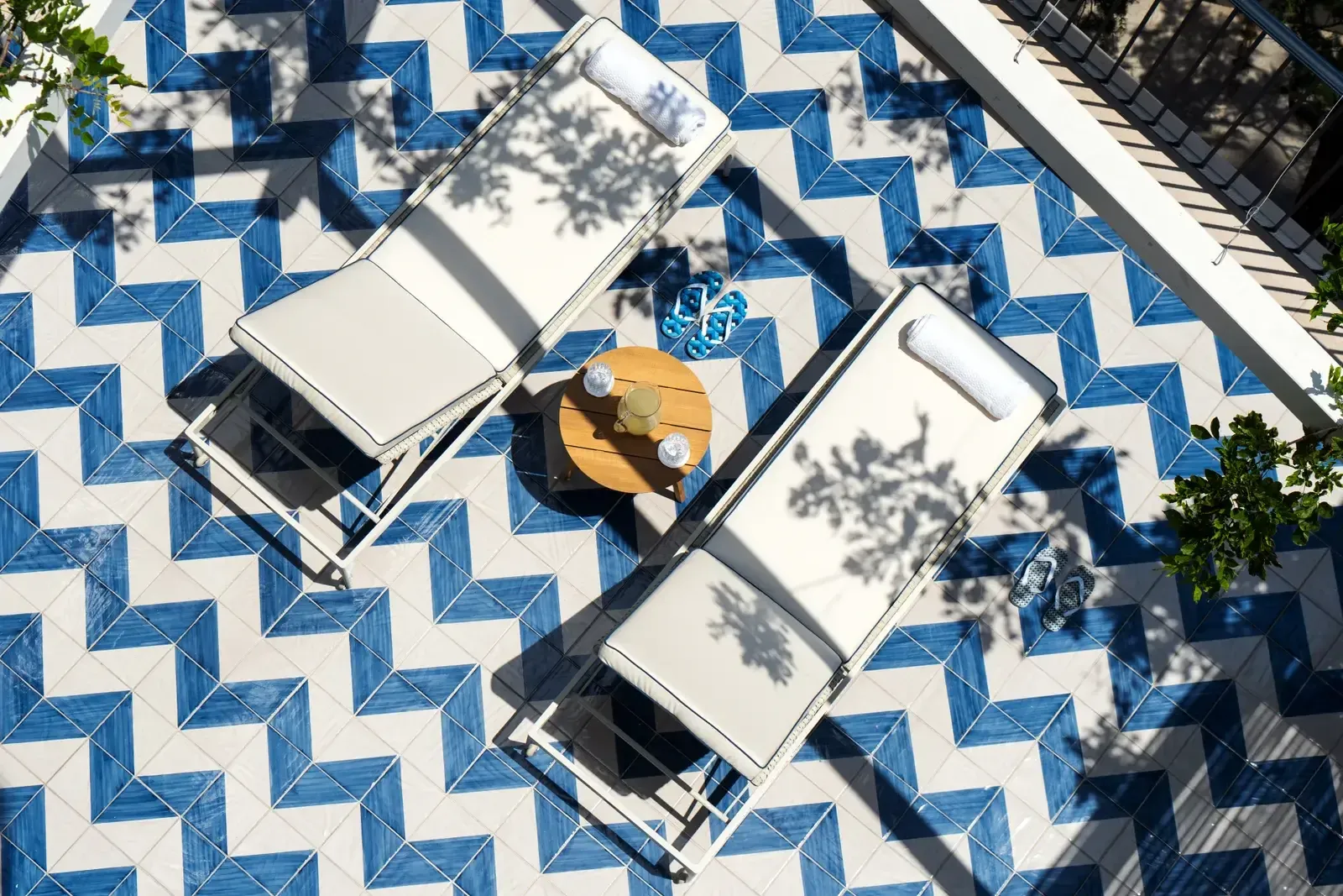 Borgo Santandrea, Europe — Overhead view of geometric blue and white tiled courtyard with loungers, golden table, and tree shadows at midday.