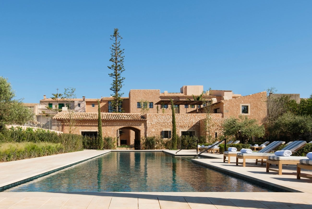 Can Ferrereta, Balearic Islands — Ochre stone villa with cypress trees, lap pool, and lounge chairs under clear sky, Mediterranean architecture.