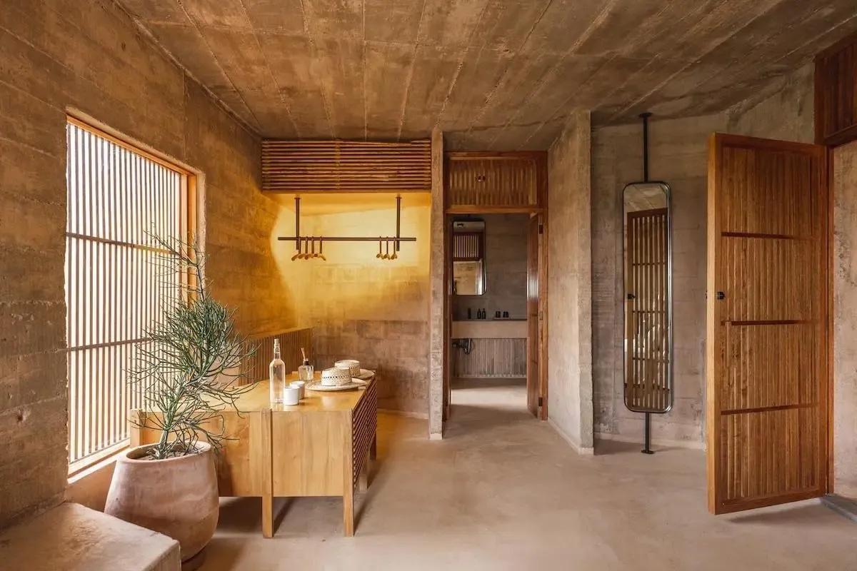 Paradero Todos Santos, Mexico — Concrete and timber interior with warm natural light filtering through slatted screens, minimalist wooden furniture, and terracotta planters.