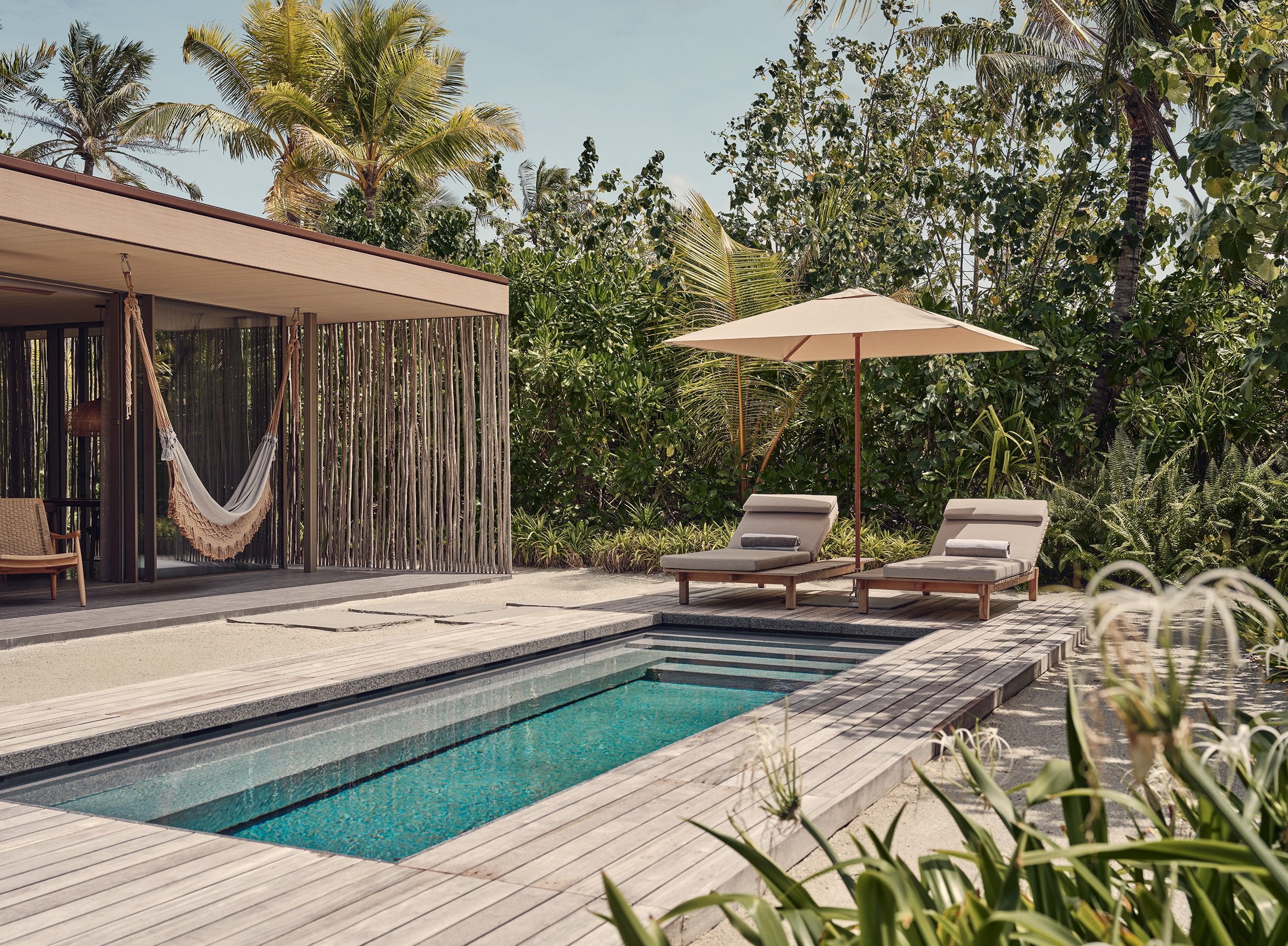 Patina Maldives, Asia — Teak pavilion with woven screens, turquoise plunge pool, wooden loungers under umbrella, tropical garden, minimalist luxury resort architecture.
