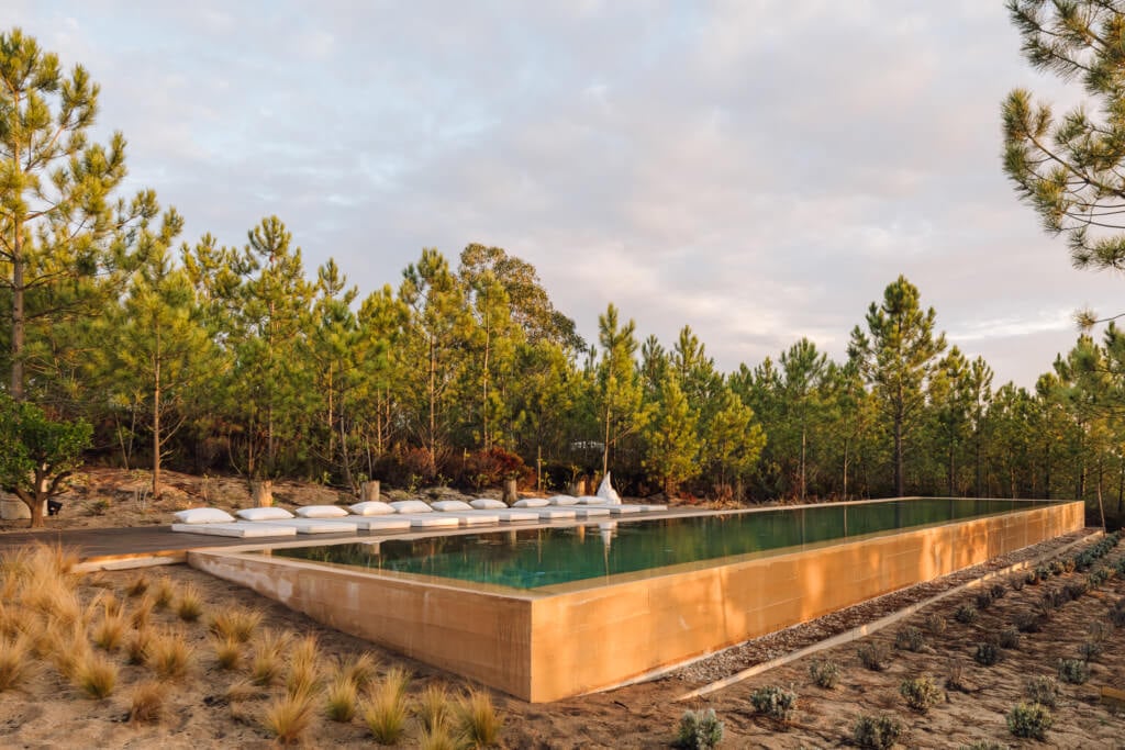 Melides Art, Portugal — Geometric concrete pool with turquoise water and golden light, pine forest backdrop, modernist luxury design in natural landscape.