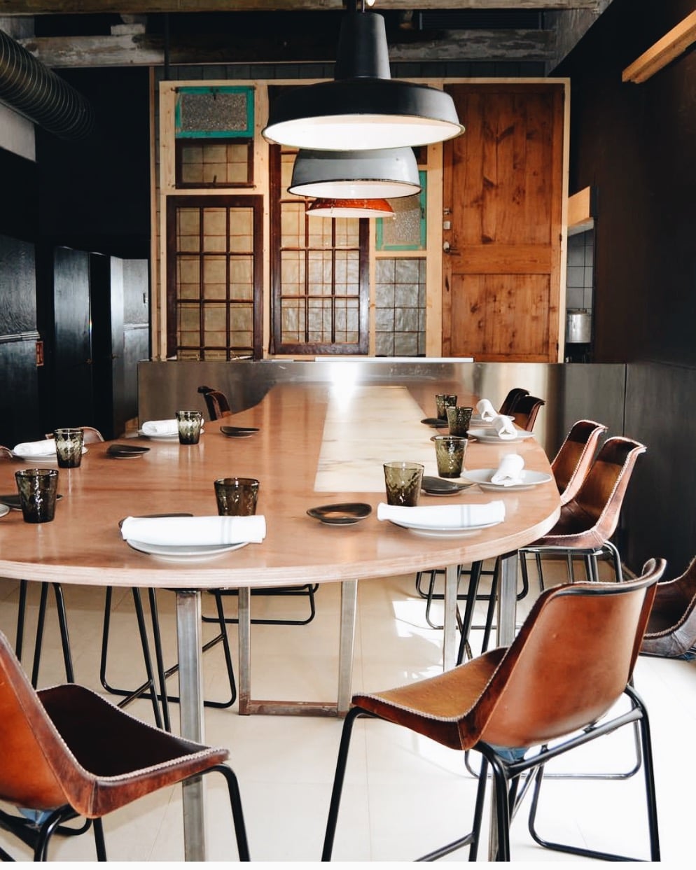 Smoix, Balearic Islands, Spain — Modern dining room with oval wood table, cognac leather chairs, industrial black pendant lights, and exposed wooden architectural elements.