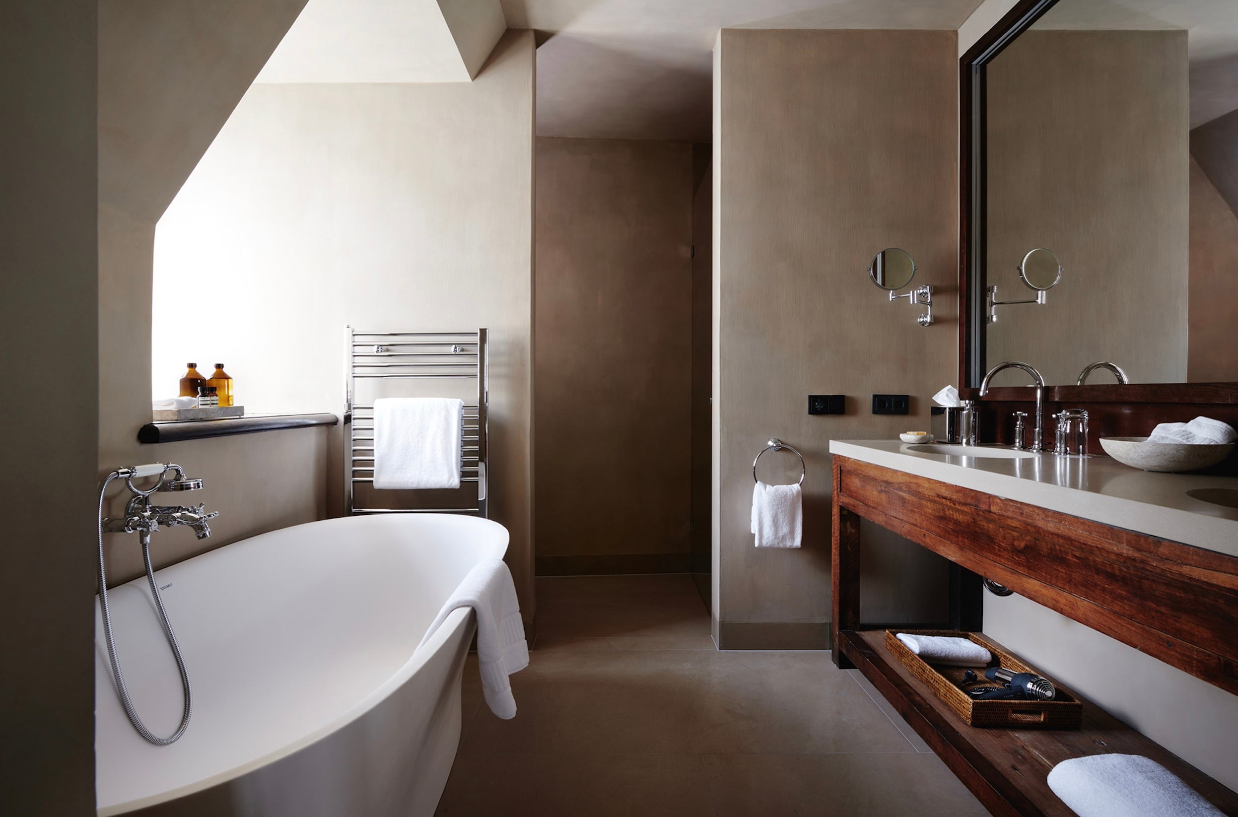 Purs, Europe — Spa bathroom with freestanding soaking tub, walnut vanity, heated towel rail, skylights, and minimalist taupe walls.
