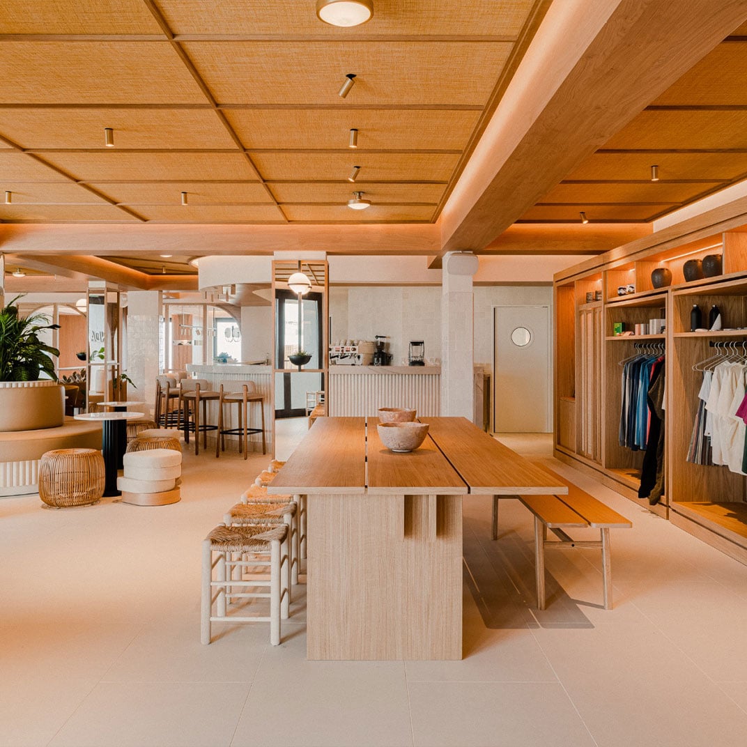 Aethos Ericeira, Portugal — Wooden ceiling and cabinetry in open-plan hospitality space with dining table, kitchen, and clothing retail displays in warm natural light.