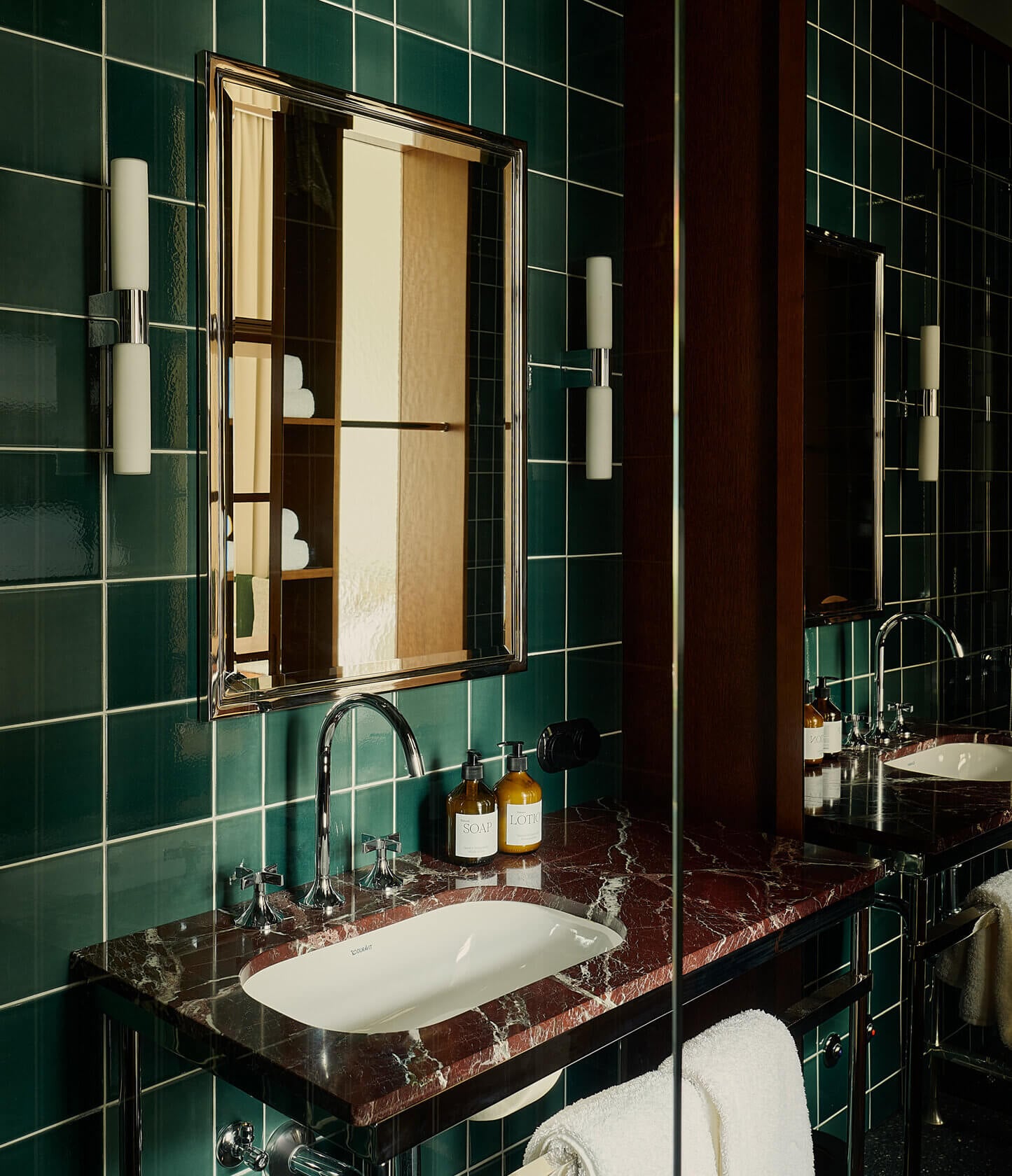 Château Royal, Europe — Emerald subway-tiled bathroom with red marble countertop, chrome fixtures, and framed mirror illuminated by cylindrical sconces.