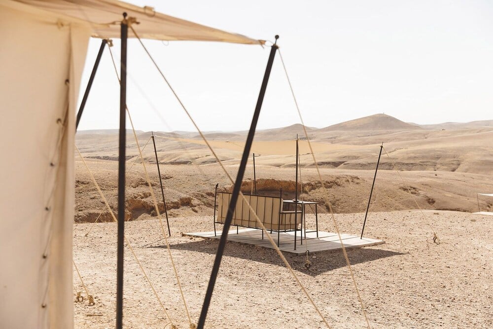 Scarabeo Camp, Africa — Minimalist desert camp with suspended canvas canopy and metal frame seating structure overlooking vast sandy landscape.