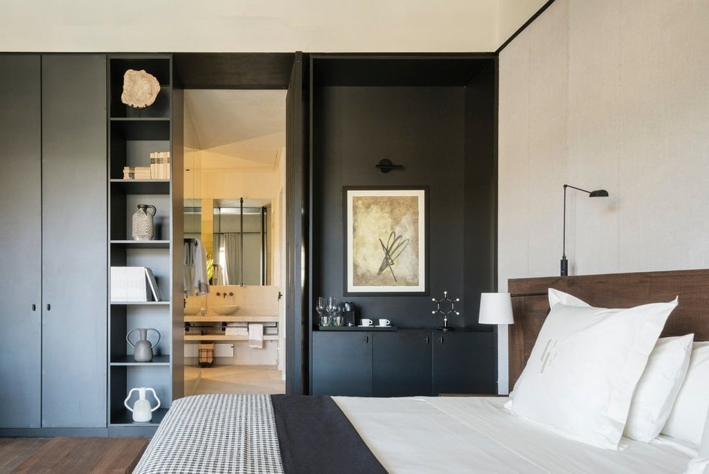 Can Ferrereta, Balearic Islands — Minimalist bedroom with walnut headboard, dark cabinetry, floating shelves, ensuite bathroom, warm lighting, contemporary luxury design