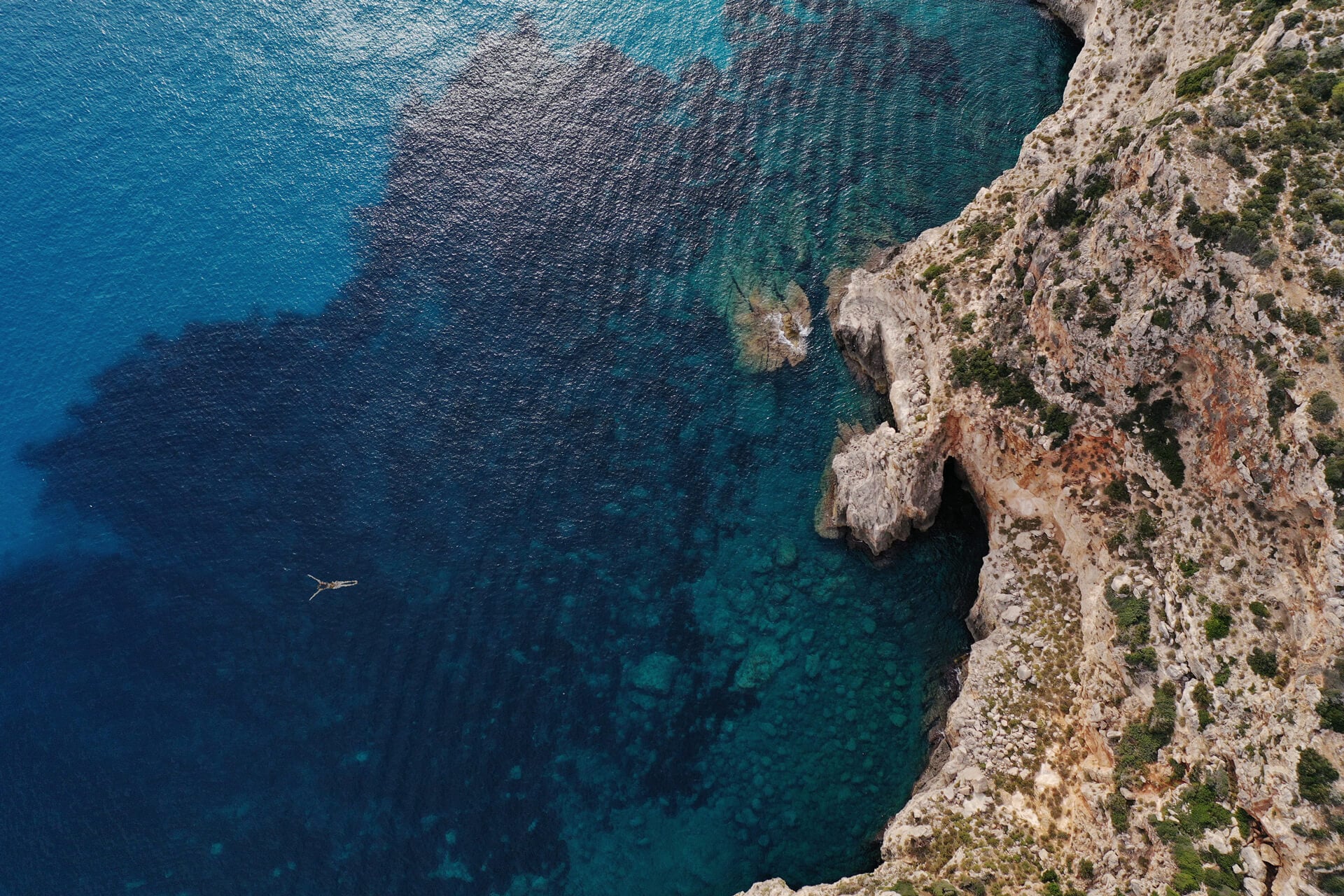 Menorca Experimental, Balearic Islands, Spain — Limestone cliff face overlooking crystalline turquoise Mediterranean waters with solitary swimmer, minimal architecture aesthetic.