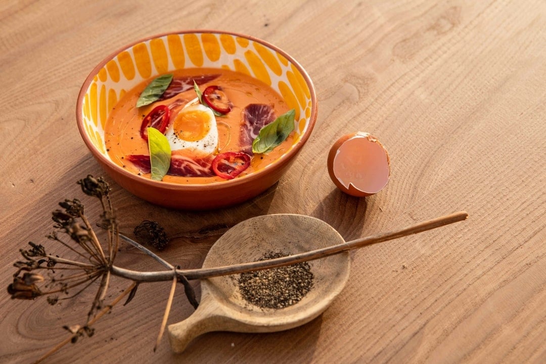Menorca Experimental, Balearic Islands, Spain — Saffron ceramic bowl with poached egg and cured meat, wooden spoon with dukkah spice, dried flowers on terracotta surface.