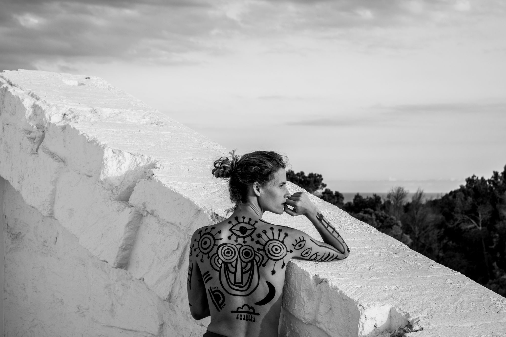 Menorca Experimental, Balearic Islands — Woman with geometric body art on white stone terrace overlooking Mediterranean landscape, black and white portrait.